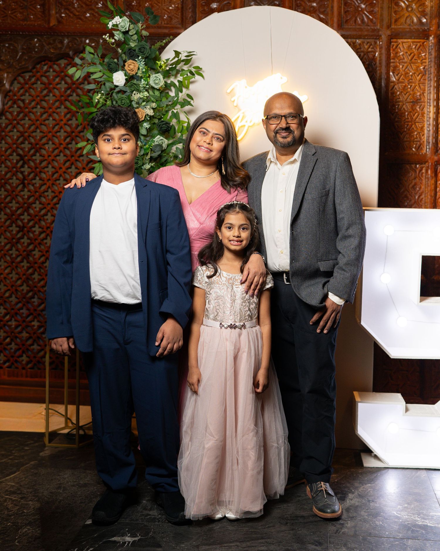 A family in coordinated formal attire poses together against a decorative wooden wall panel for a portrait session.