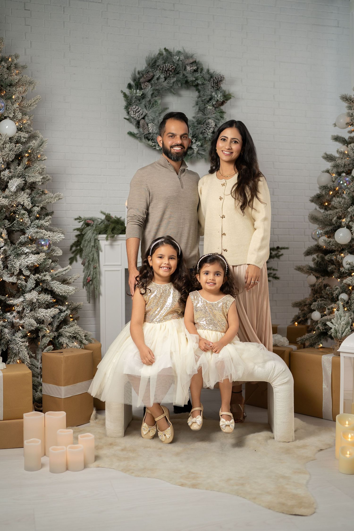 Holiday portrait session with a family in neutral tones sitting by decorated Christmas trees and candles.
