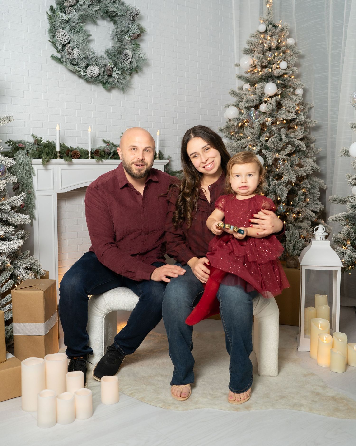 Relaxed family portrait in matching burgundy tops with Christmas trees and decorative candles.
