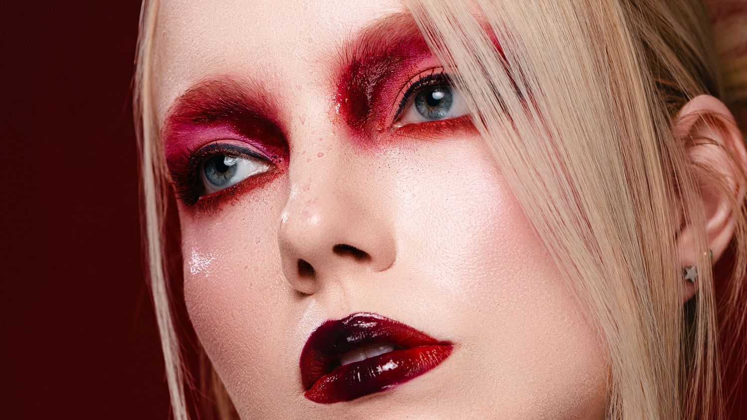 Woman with dramatic red and black Halloween vampire makeup, bold crimson eyeshadow, and dark glossy lips.