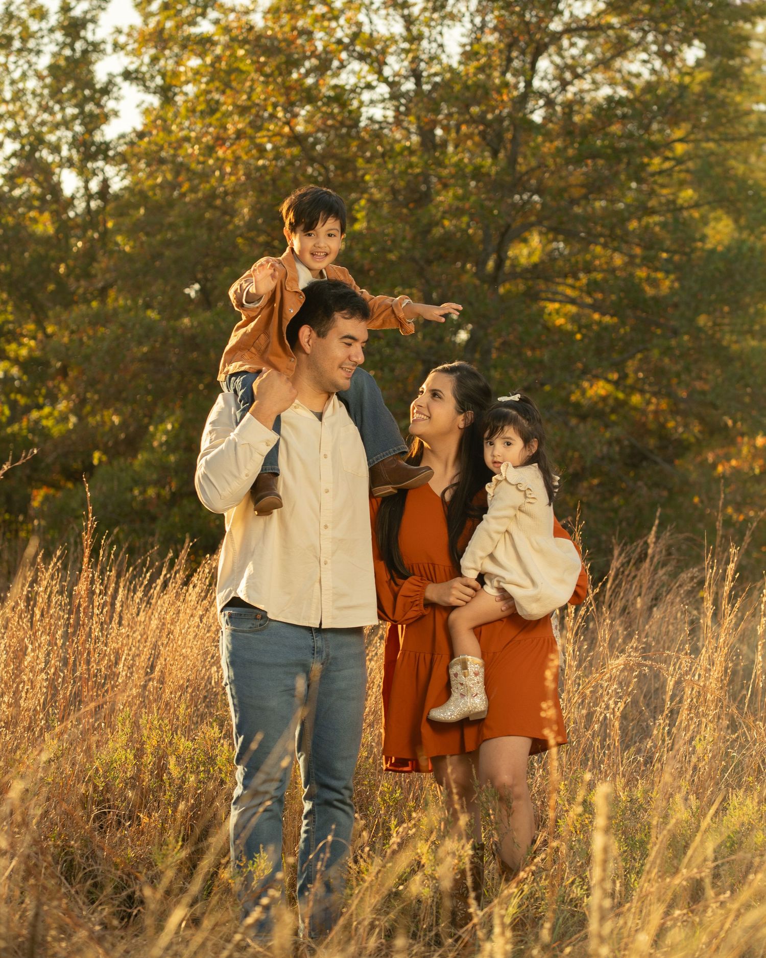 Family walking through tall golden grass during autumn sunset.