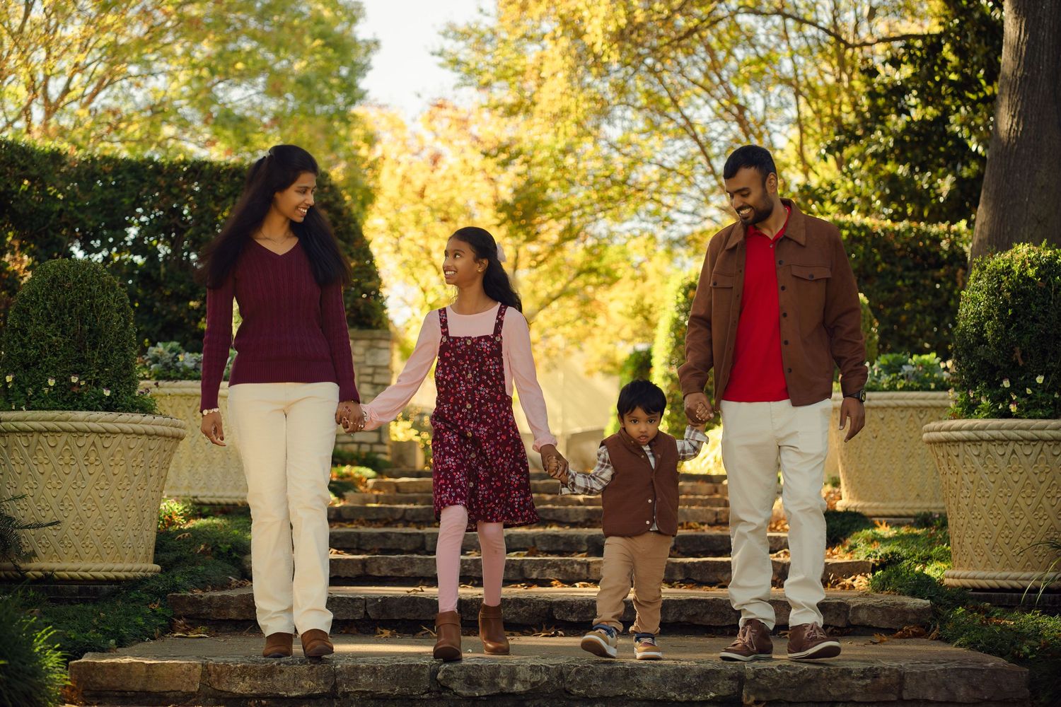 Family walking together along a garden path surrounded by golden fall foliage.