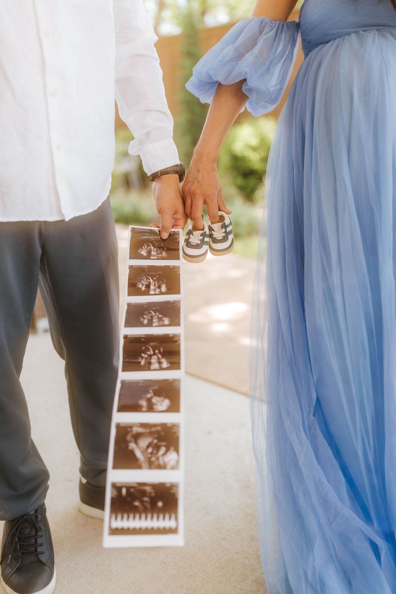 Couple holding ultrasound strip and tiny baby shoes during pregnancy announcement photoshoot outdoors.