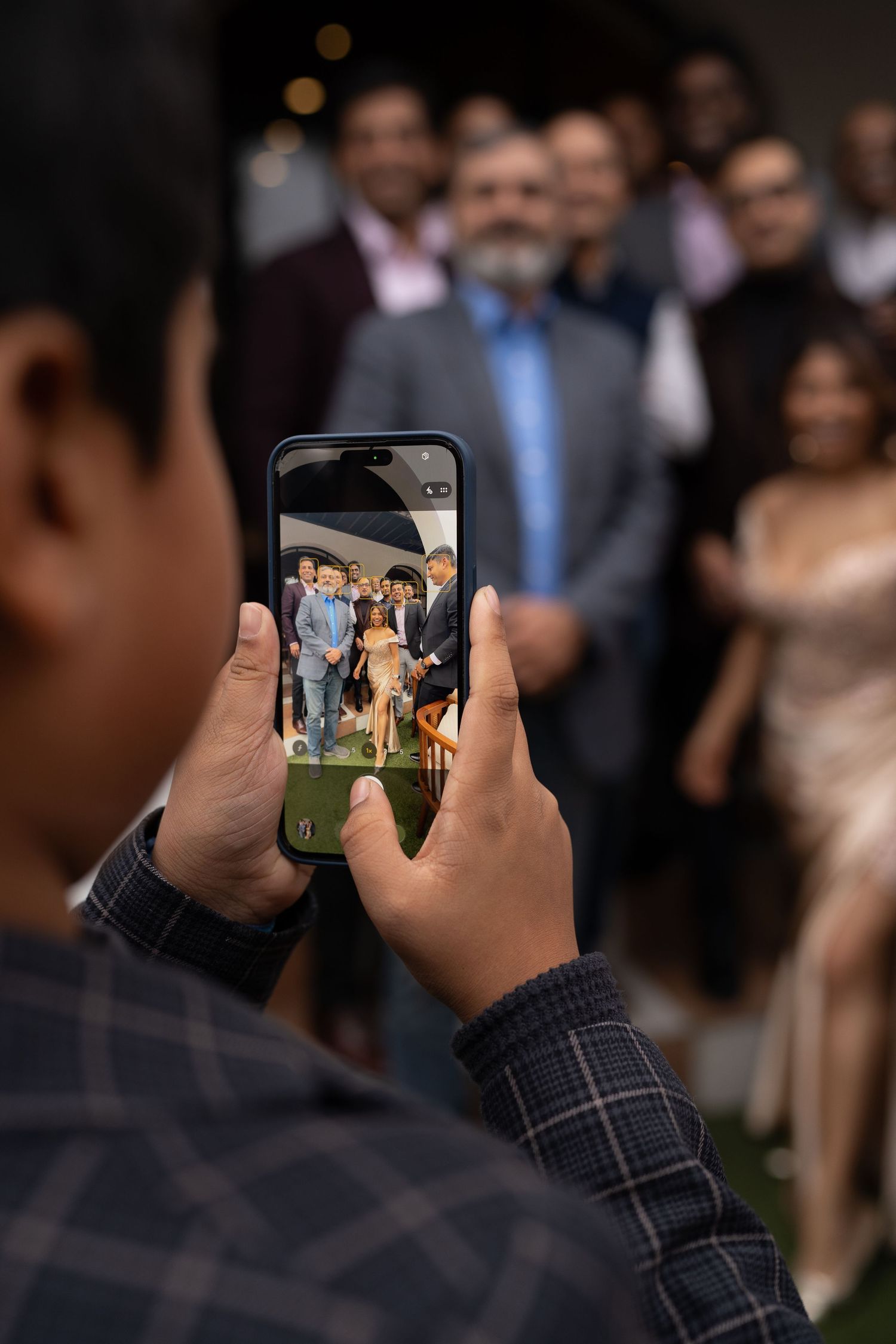 Someone takes a photo of a couple at a wedding reception with a smartphone camera in a dimly lit venue.