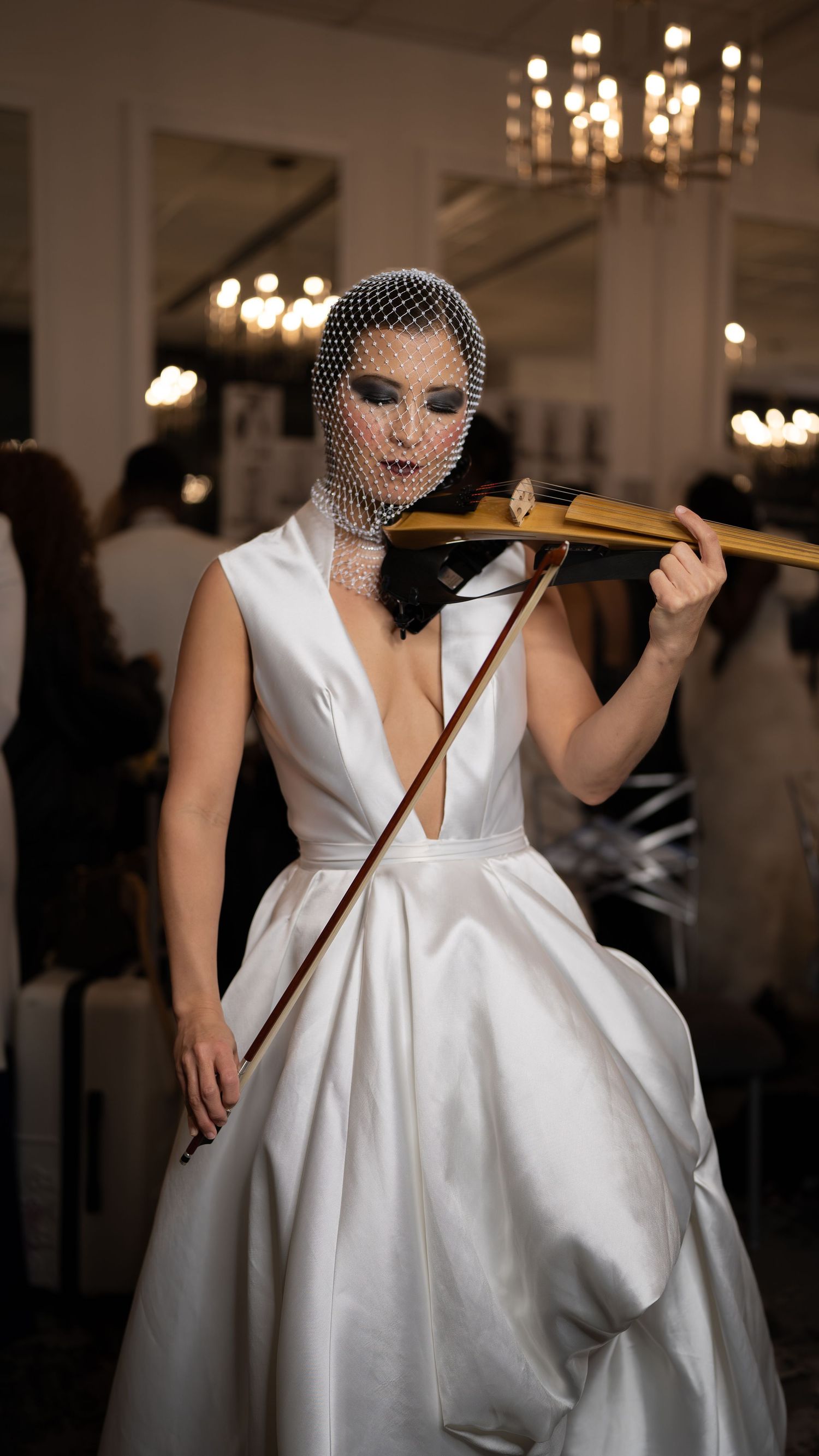 A bride in a classic white satin ball gown and birdcage veil poses playfully with a wooden pole in an elegant venue.
