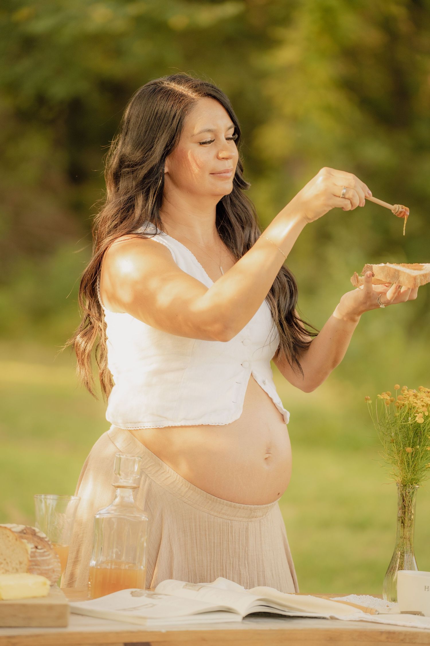 Maternity photoshoot in a sunny garden with white dress and flowy fabric creating an ethereal outdoor scene.