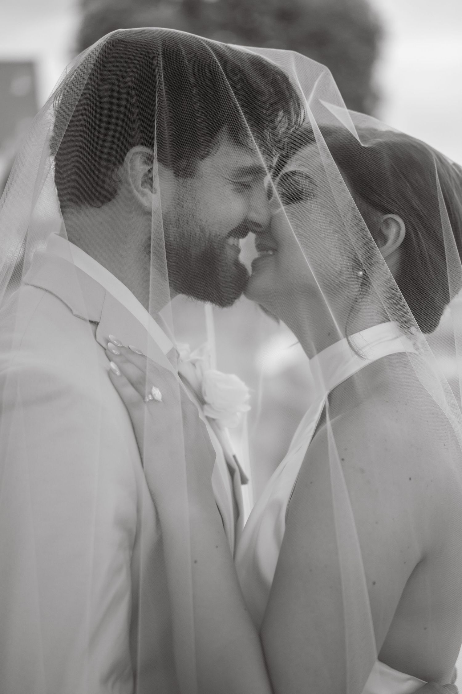 Black and white photo of a bride and groom sharing an intimate moment under a wedding veil.