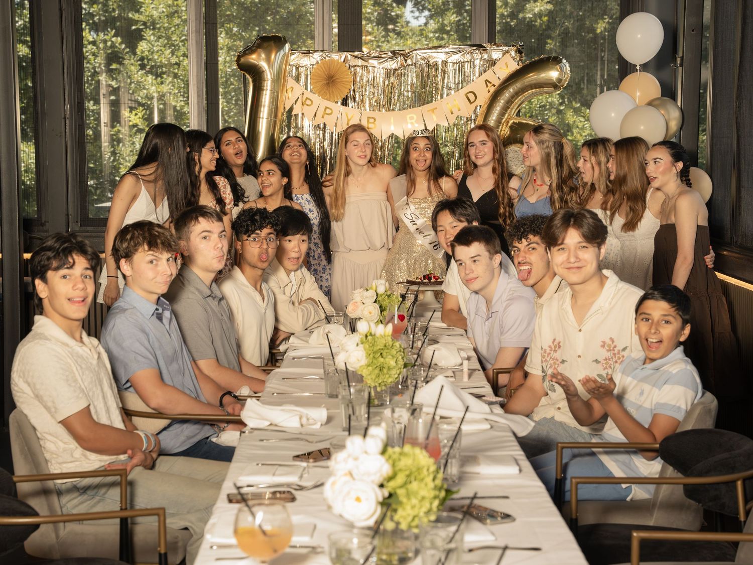 Large group of teens celebrating a 16th birthday party at an elegant restaurant with gold balloon decorations.