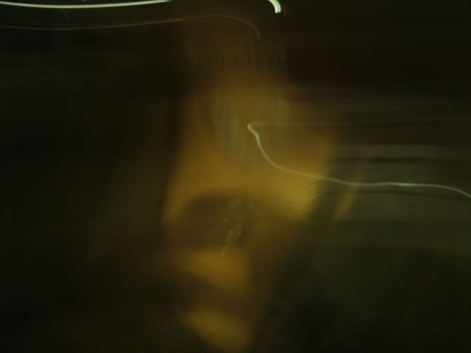 Blurred abstract portrait with golden light streaks illuminating a chest with a cross in dark, moody tones.