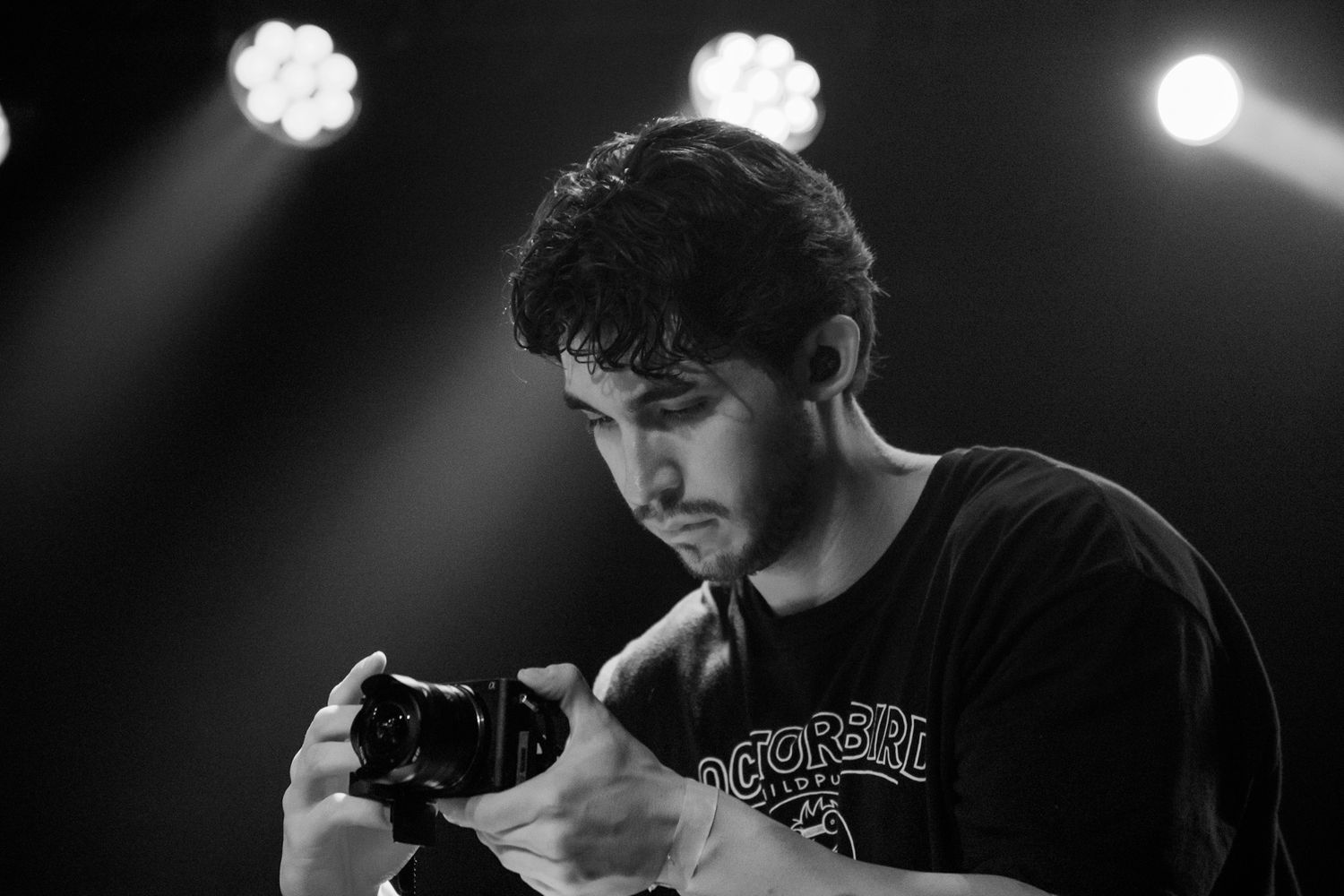 Black and white photo of a young man reviewing photos on a camera under stage lighting.