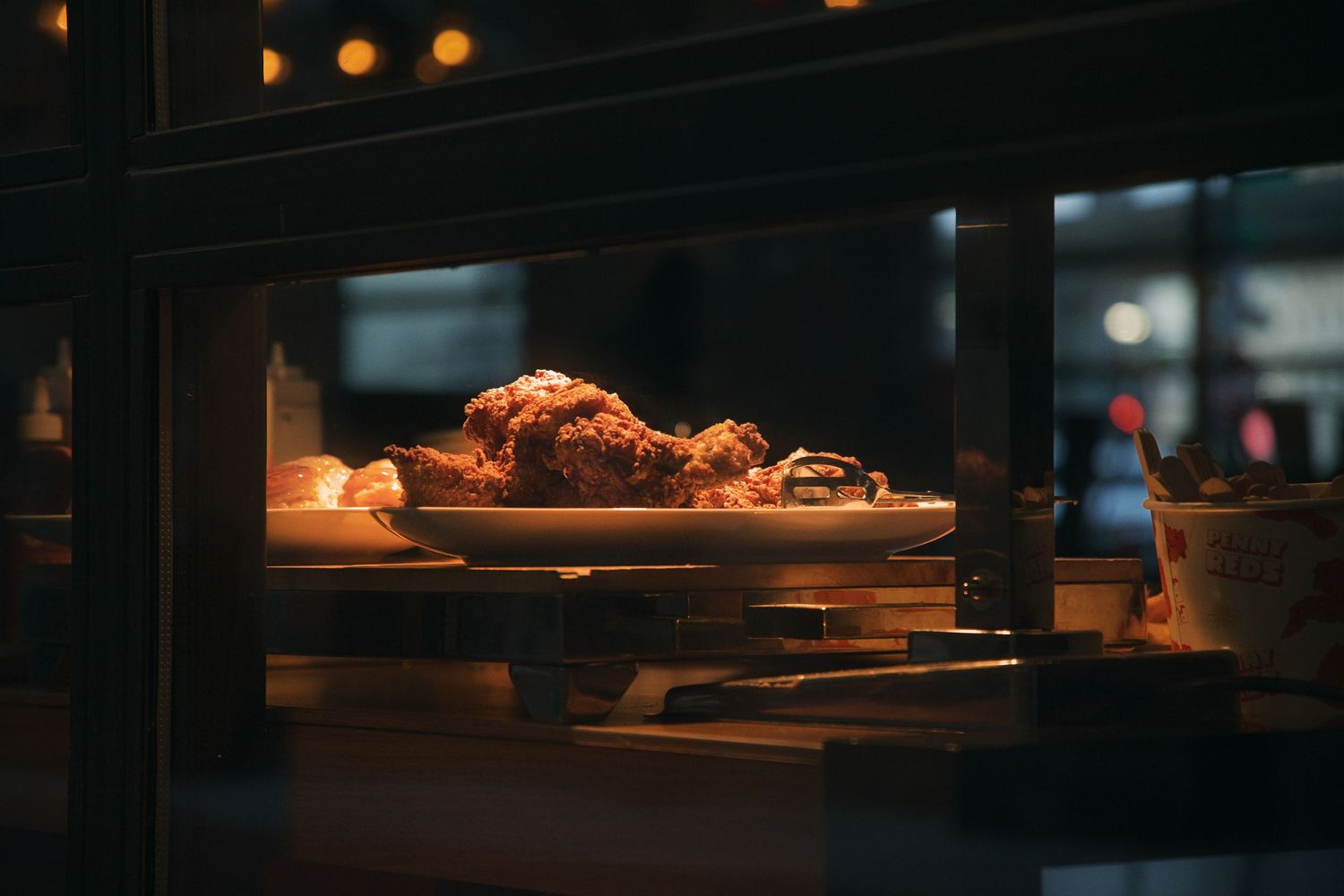 Fried chicken on a white plate displayed in a warmly lit restaurant kitchen window at night. Taken in an alleyway in downtown Detroit.