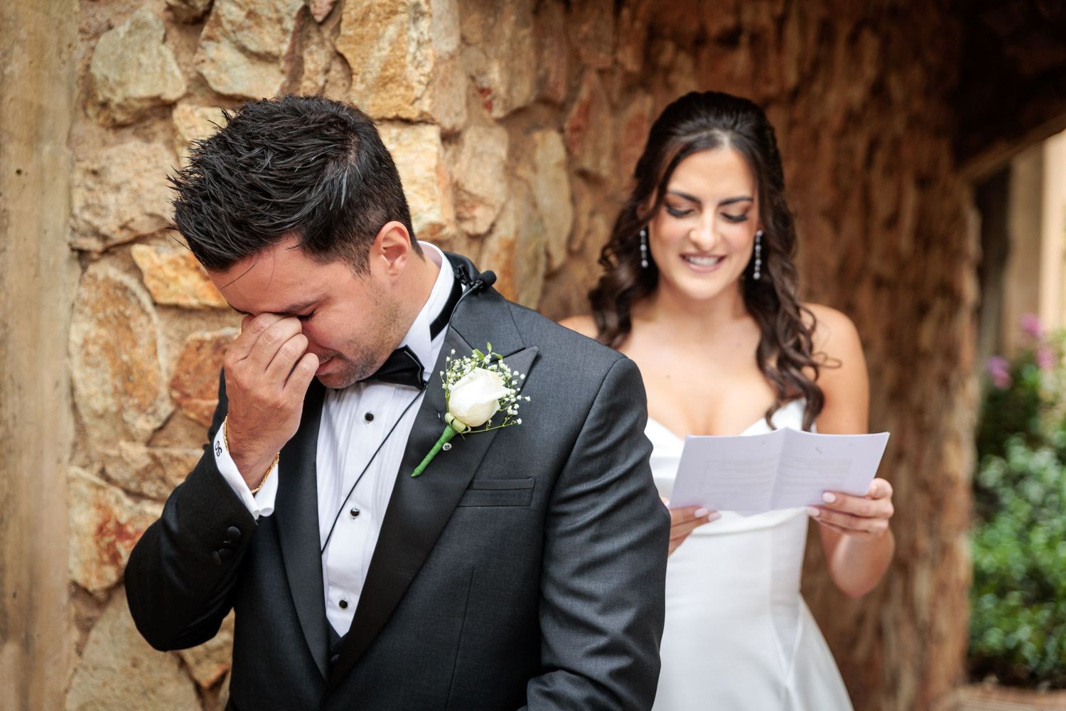 A wedding couple shares an intimate moment while reading letters in front of a rustic stone wall.