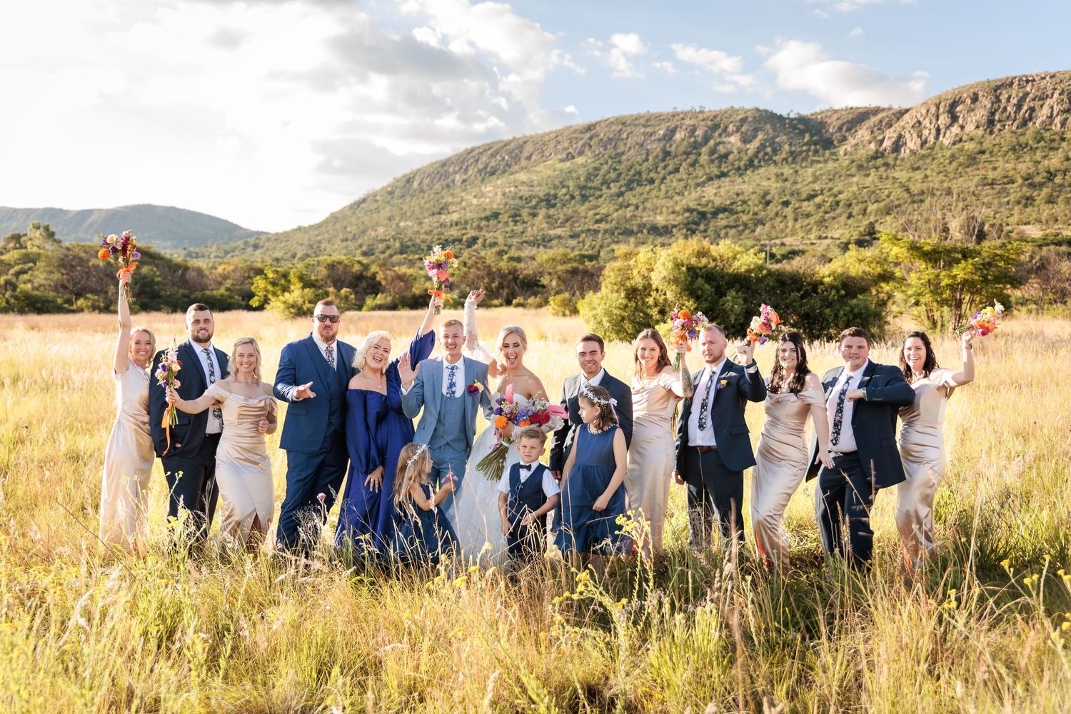 Wedding party in navy blue attire poses together in a scenic mountain landscape at sunset.
