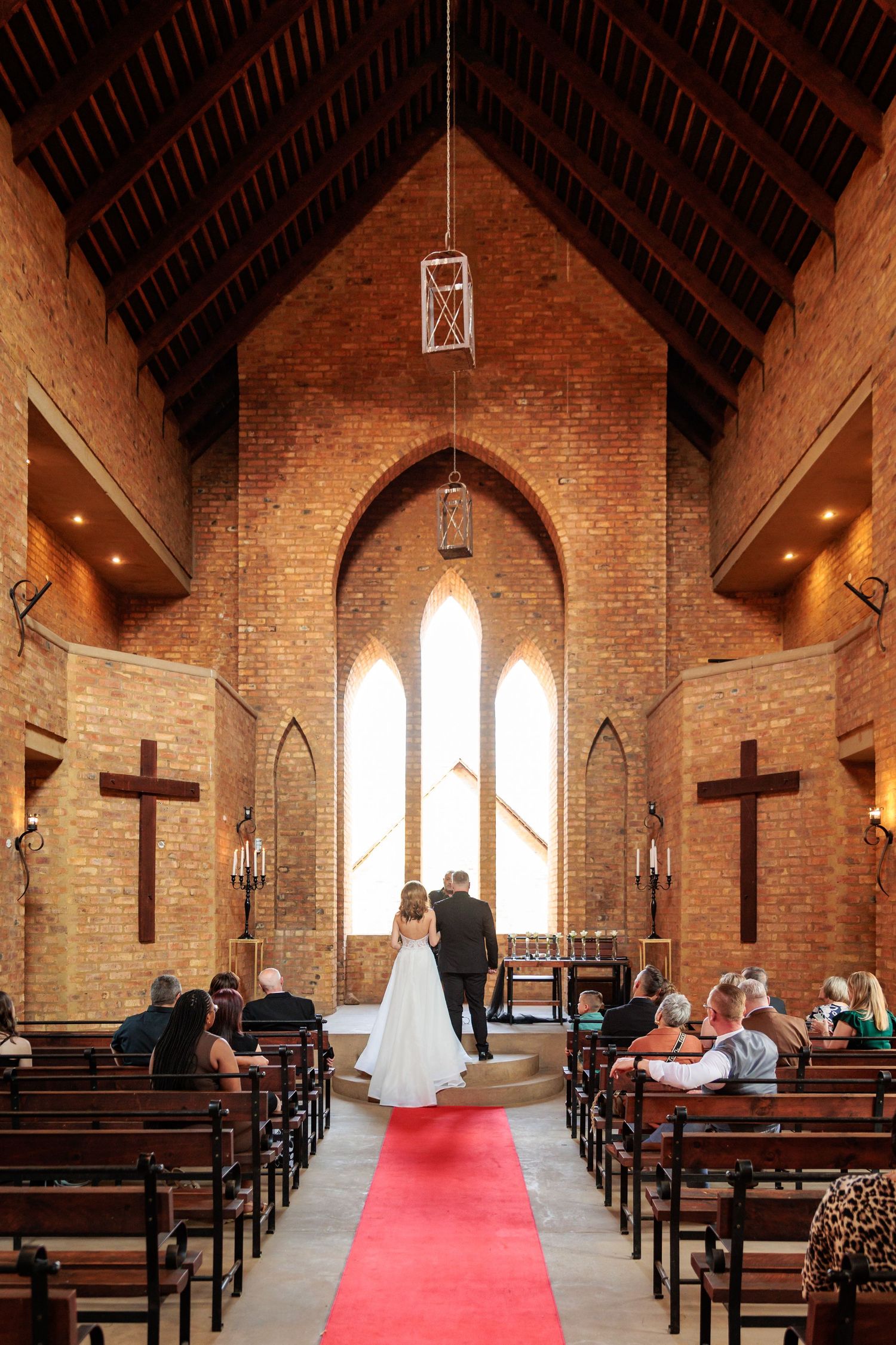 Interior view of a brick church sanctuary with wooden pews, arched windows, and a red carpet leading to the altar.