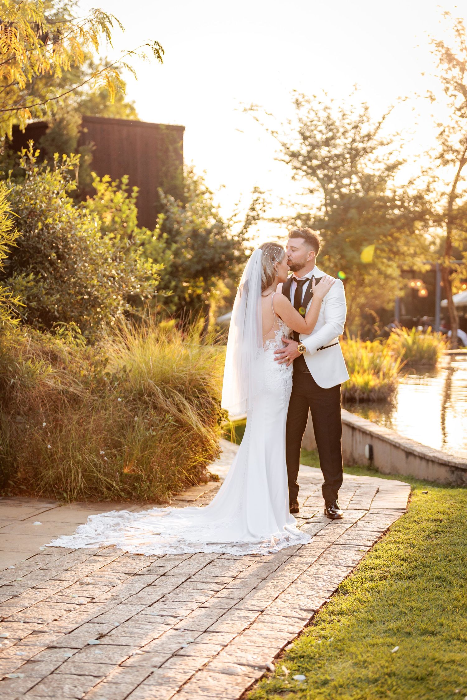 A romantic wedding couple shares tender moments at sunset in a garden setting with stone pathways and golden light.