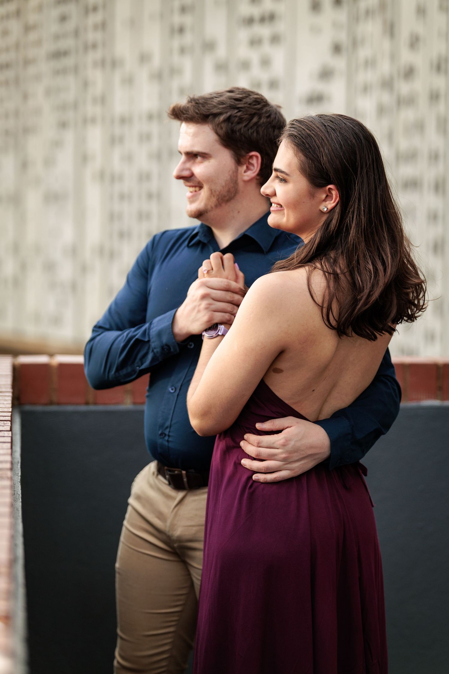 A couple in blue and burgundy clothing embraces while laughing together in a romantic outdoor photoshoot.
