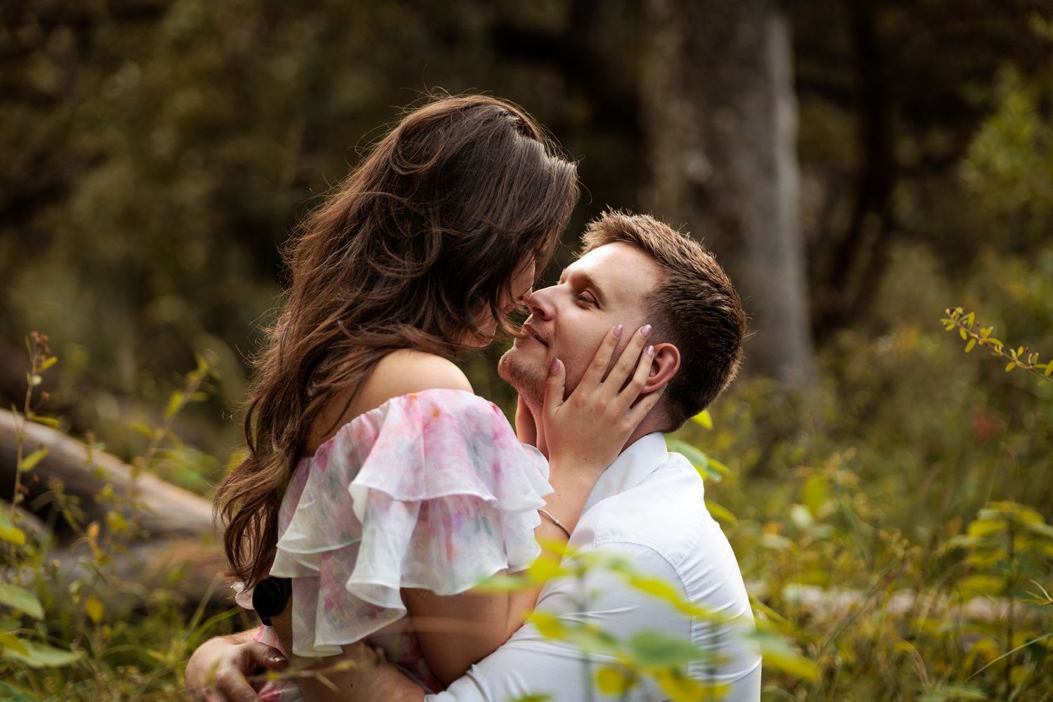 A couple in white and yellow clothing share a romantic kiss outdoors in a natural setting.
