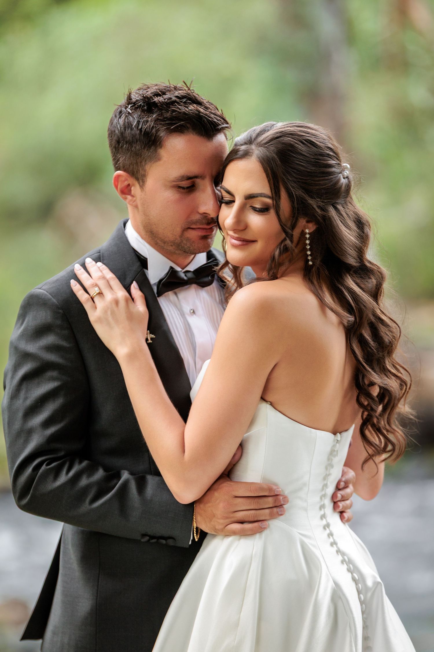 A romantic wedding couple embraces outdoors in a garden setting, sharing intimate moments in formal attire.