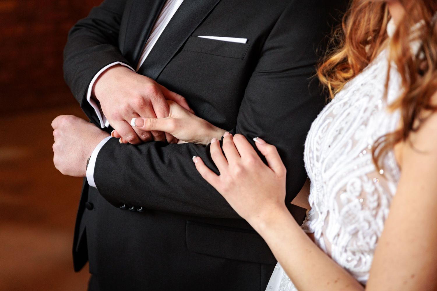 A romantic wedding couple dances together in formal attire during their first dance at an indoor reception.