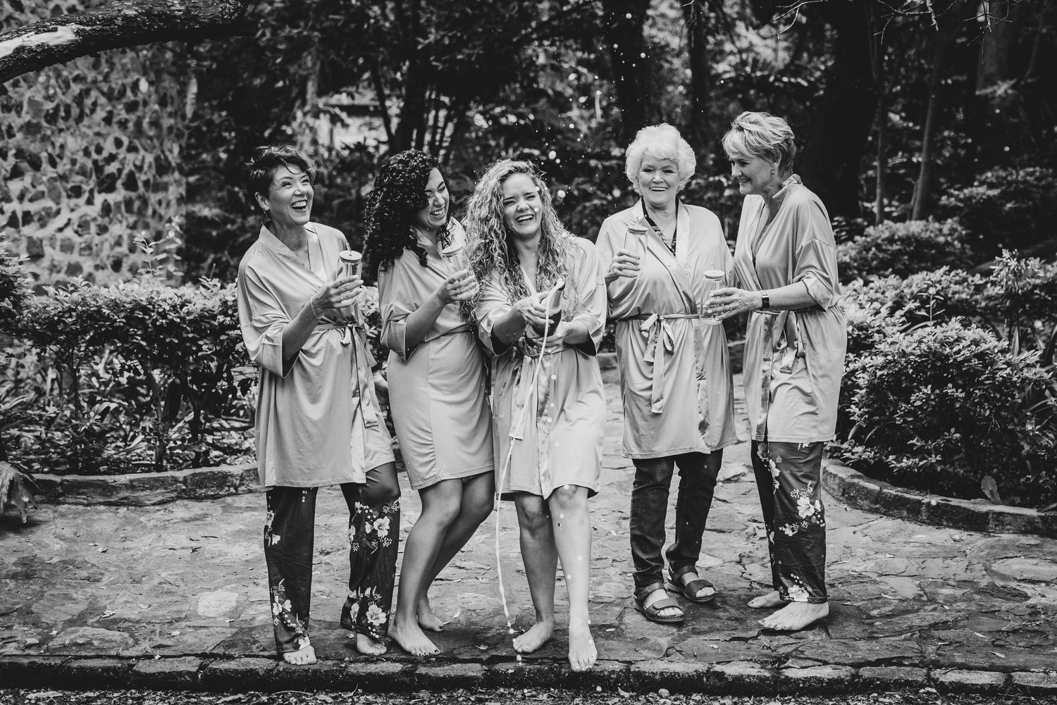 Black and white photo of wedding party walking through a garden path.