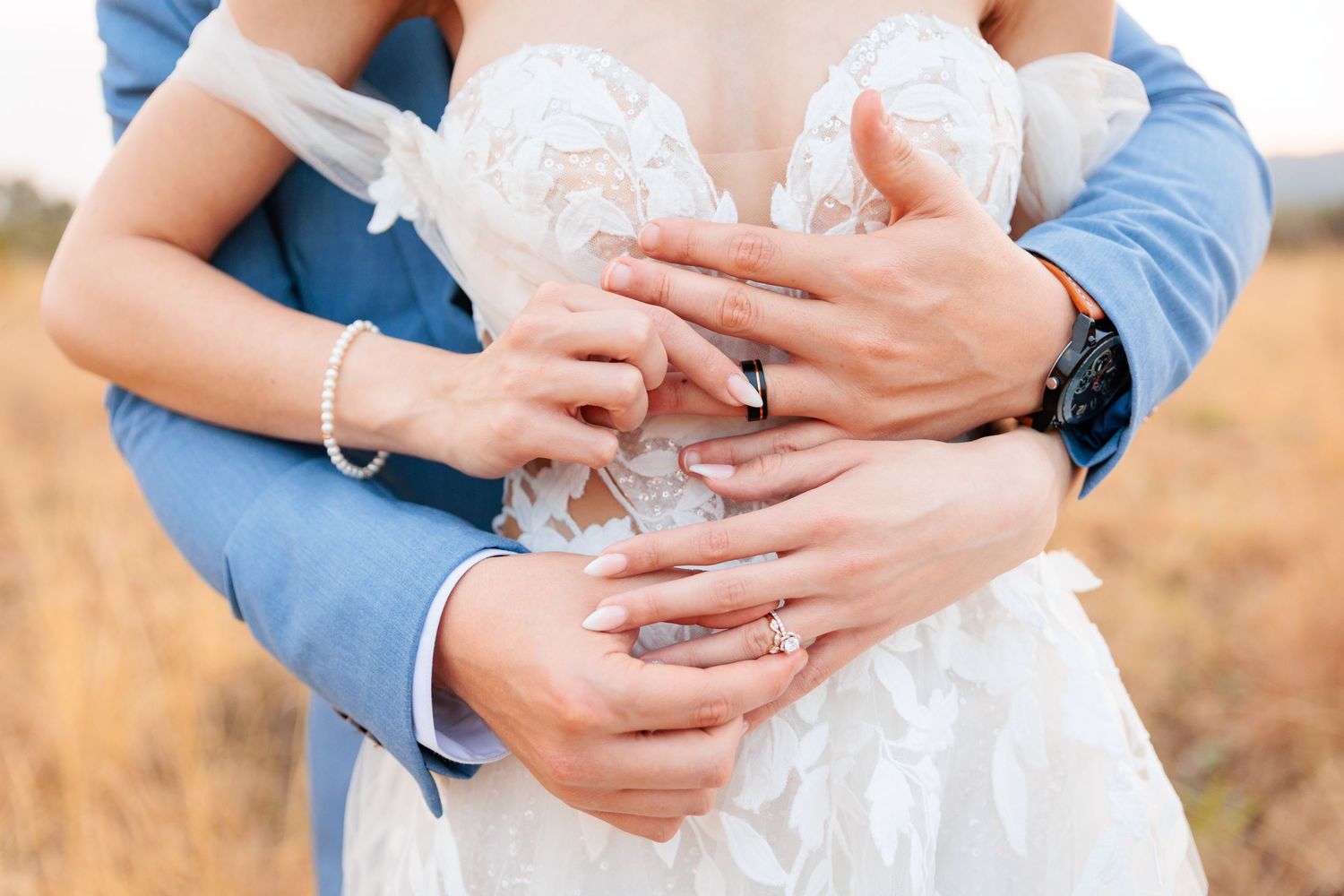 A couple shares an intimate moment in a sunlit meadow wearing blue and white attire.