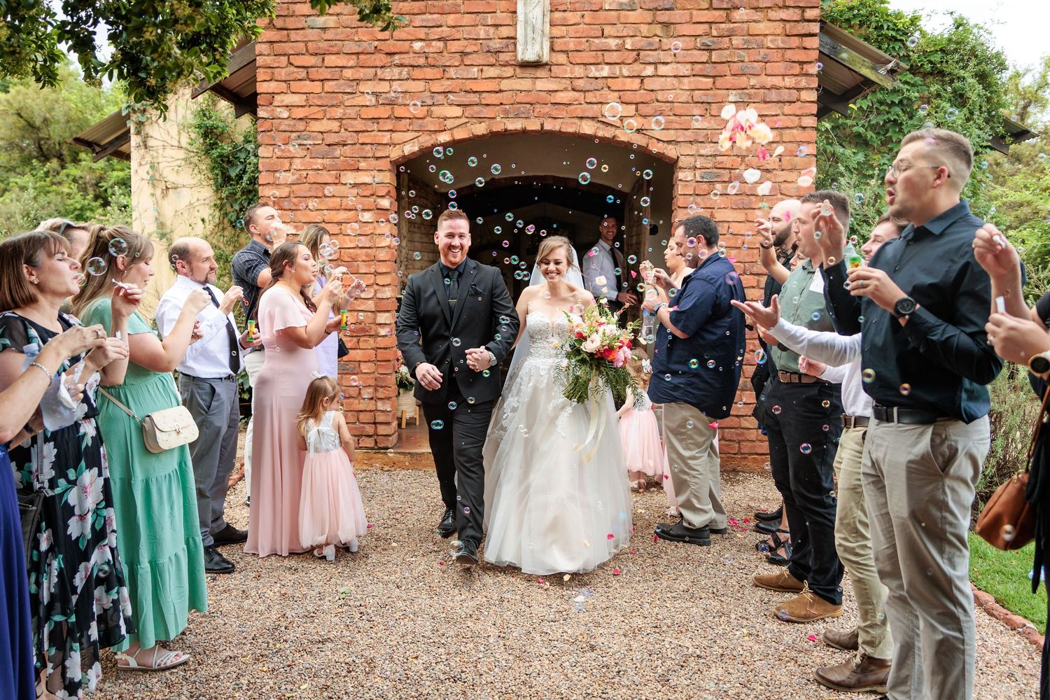 Wedding guests throw confetti during outdoor celebration at rustic brick venue.