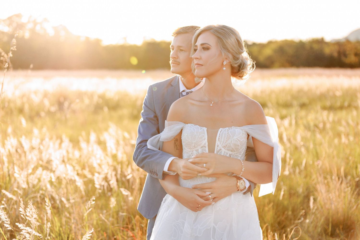 Couple embraces in golden sunlit field during sunset photoshoot wearing formal attire.