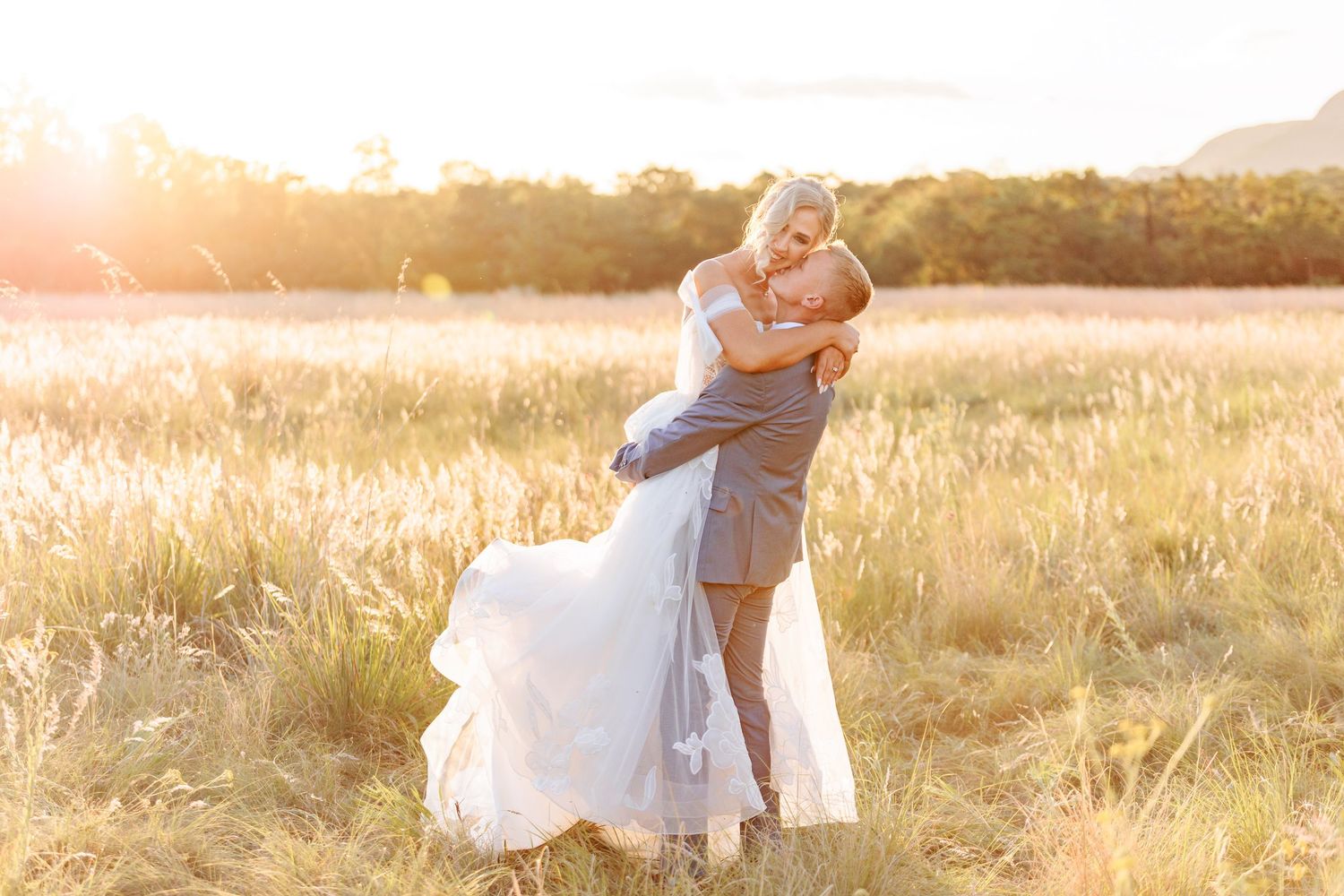 A couple embraces in a golden sunlit field during sunset creating a romantic silhouette against the warm sky.