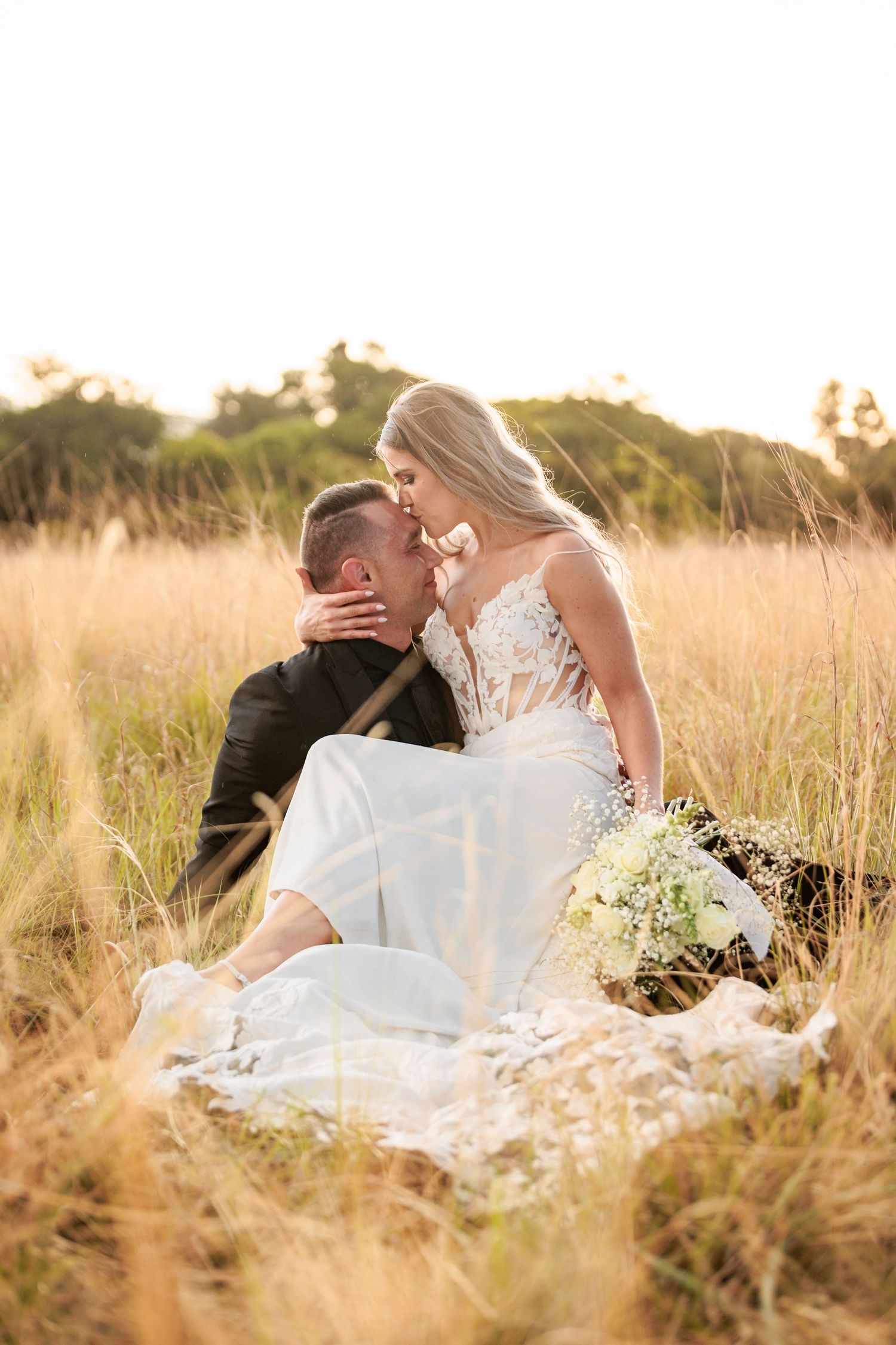 A romantic couple embraces in a golden field of tall grass during sunset.