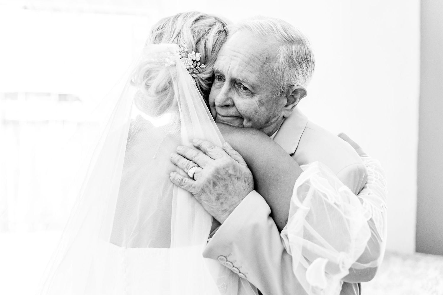 Black and white photo of a bride and elderly man sharing a tender embrace on her wedding day.