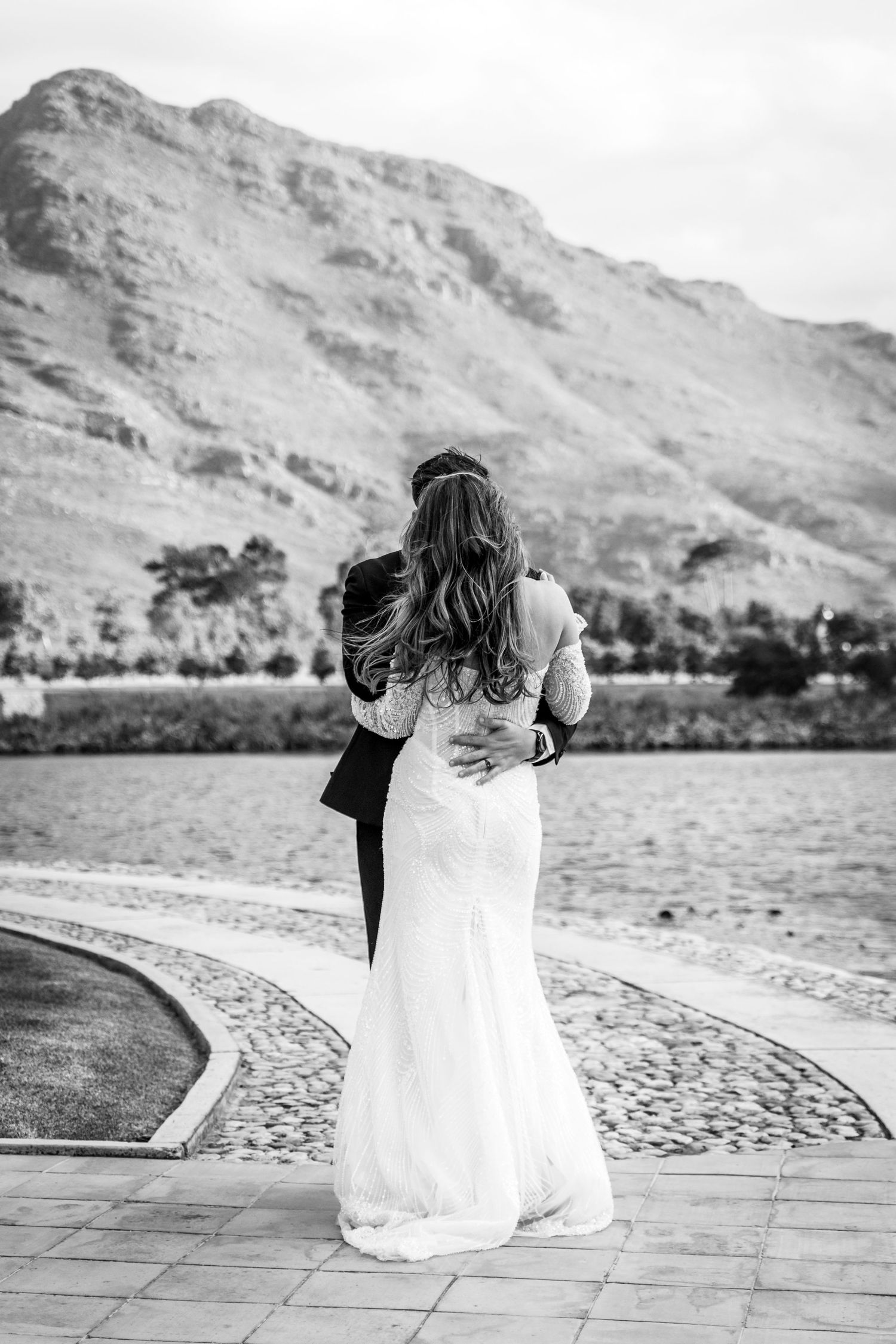 A romantic black and white wedding photo shows a couple embracing while overlooking a scenic mountain landscape.