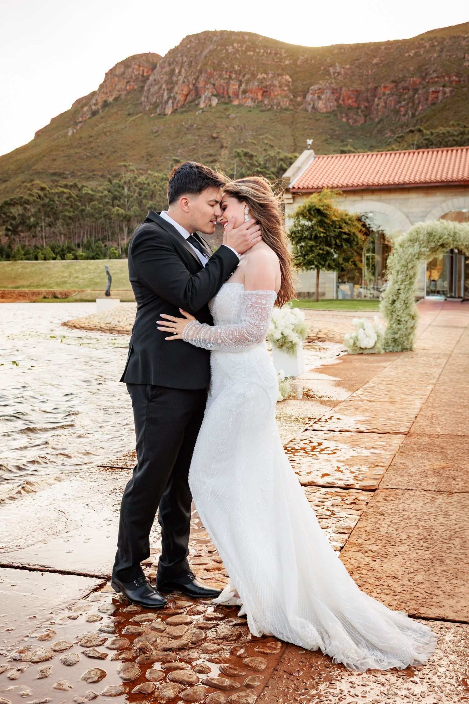 A romantic wedding couple shares an intimate moment against a scenic mountain backdrop at sunset.