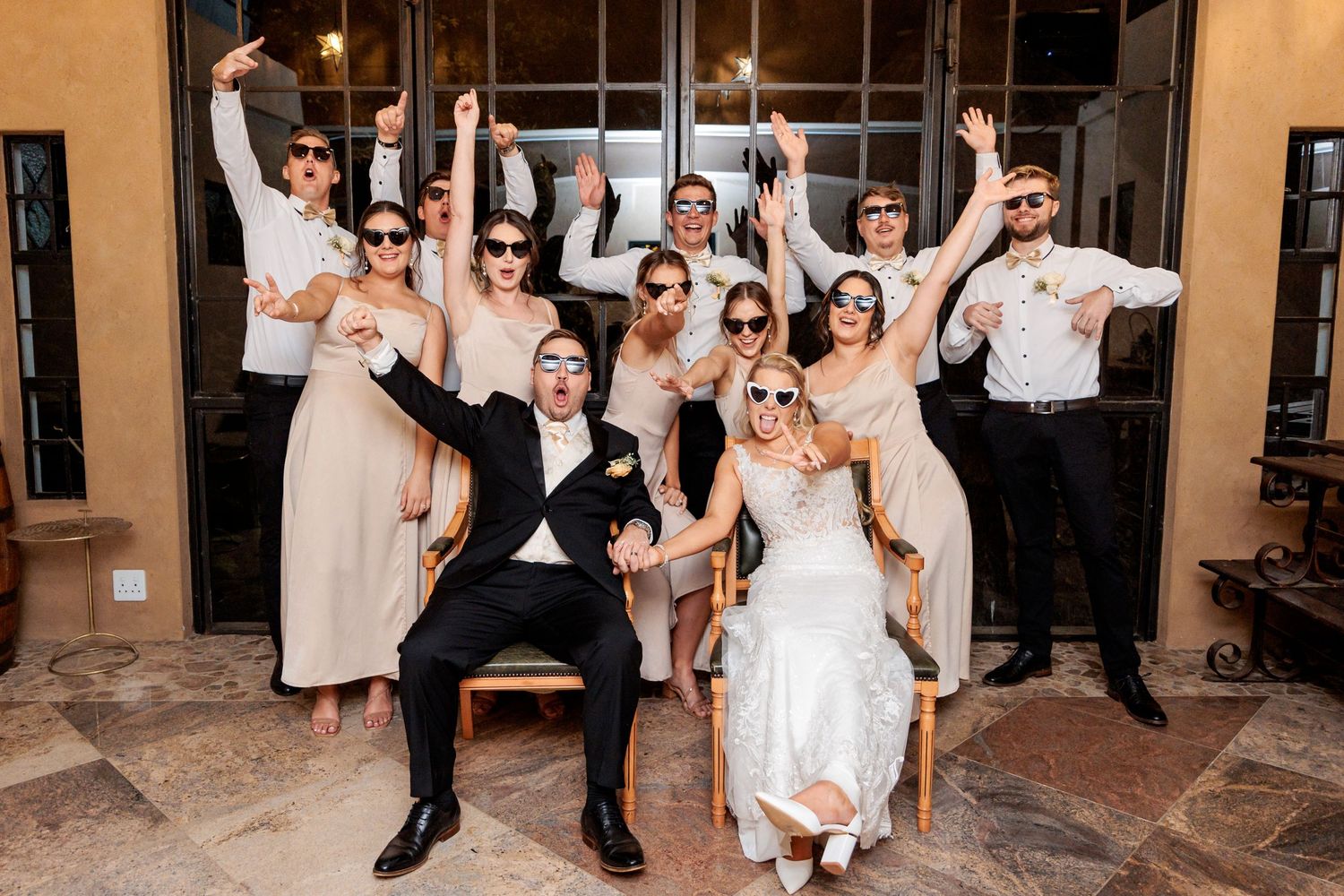 Wedding party celebrates with joyful dance moves in formal attire at an elegant indoor venue.