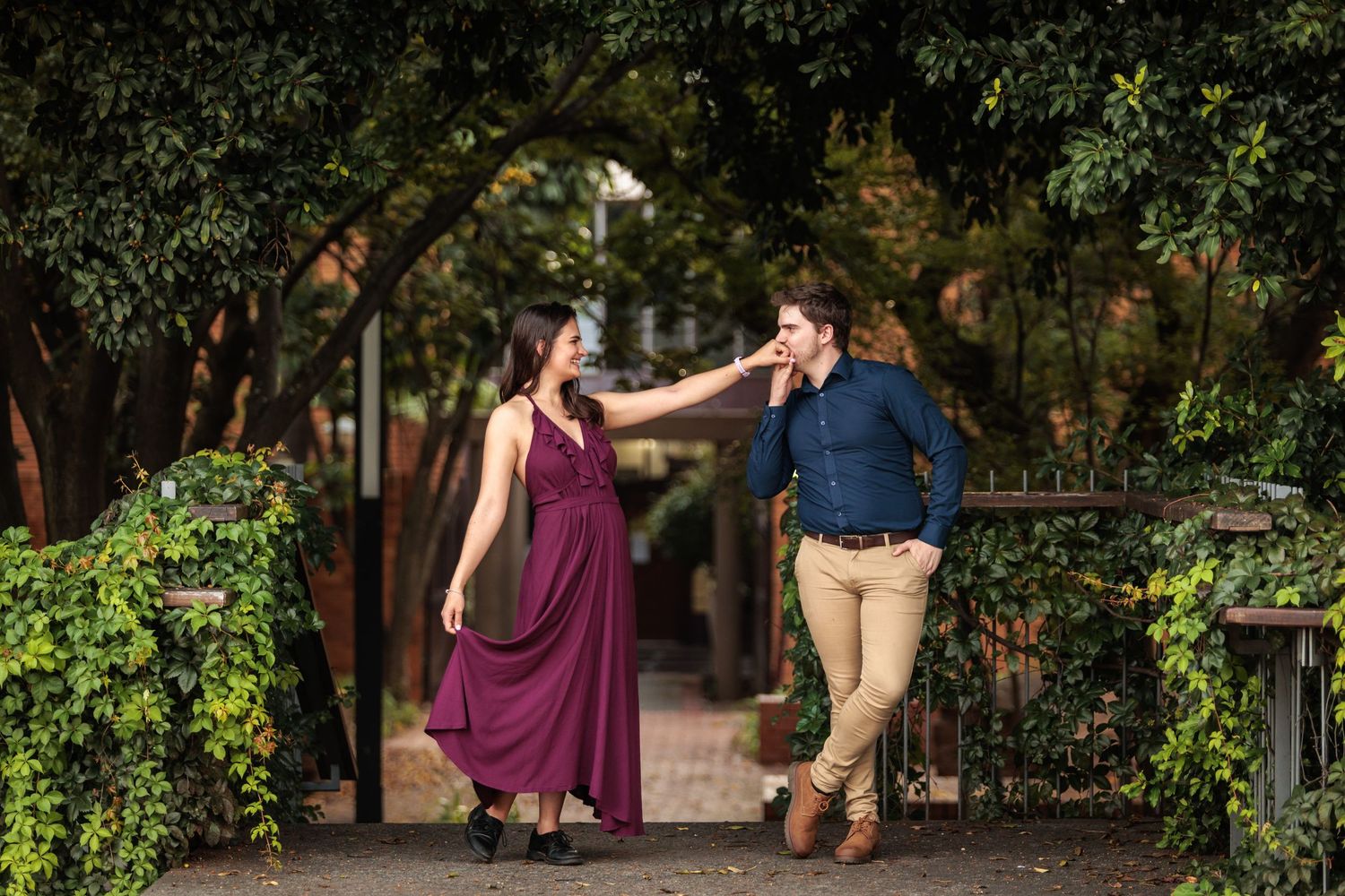 A couple dances together on a tree-lined path in an outdoor garden setting during a romantic photoshoot session.