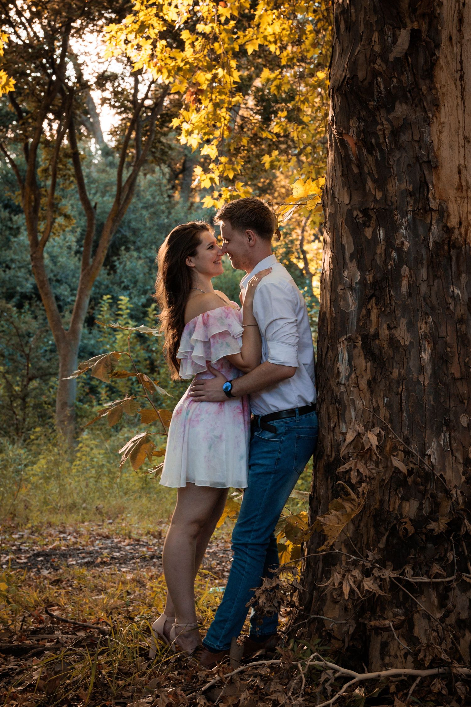 A romantic couple shares tender moments against a backdrop of golden autumn trees in a forest setting.