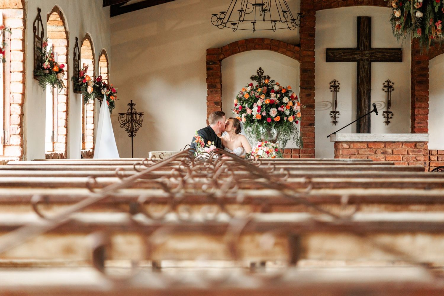 A church wedding ceremony with white floral arrangements and sunlight streaming through stained glass windows.