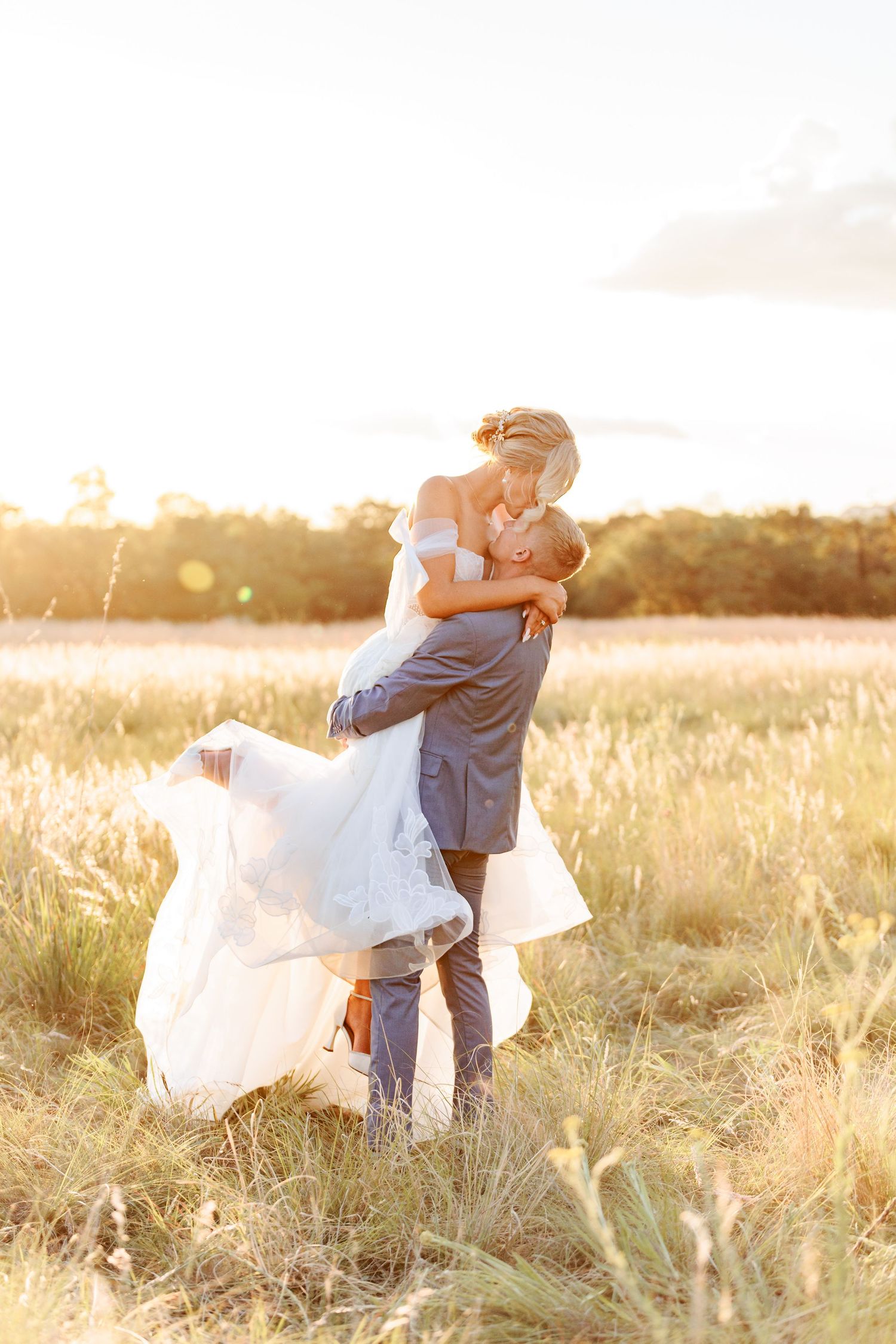 A couple embraces in a golden sunlit field during sunset creating a romantic silhouette against the warm sky.
