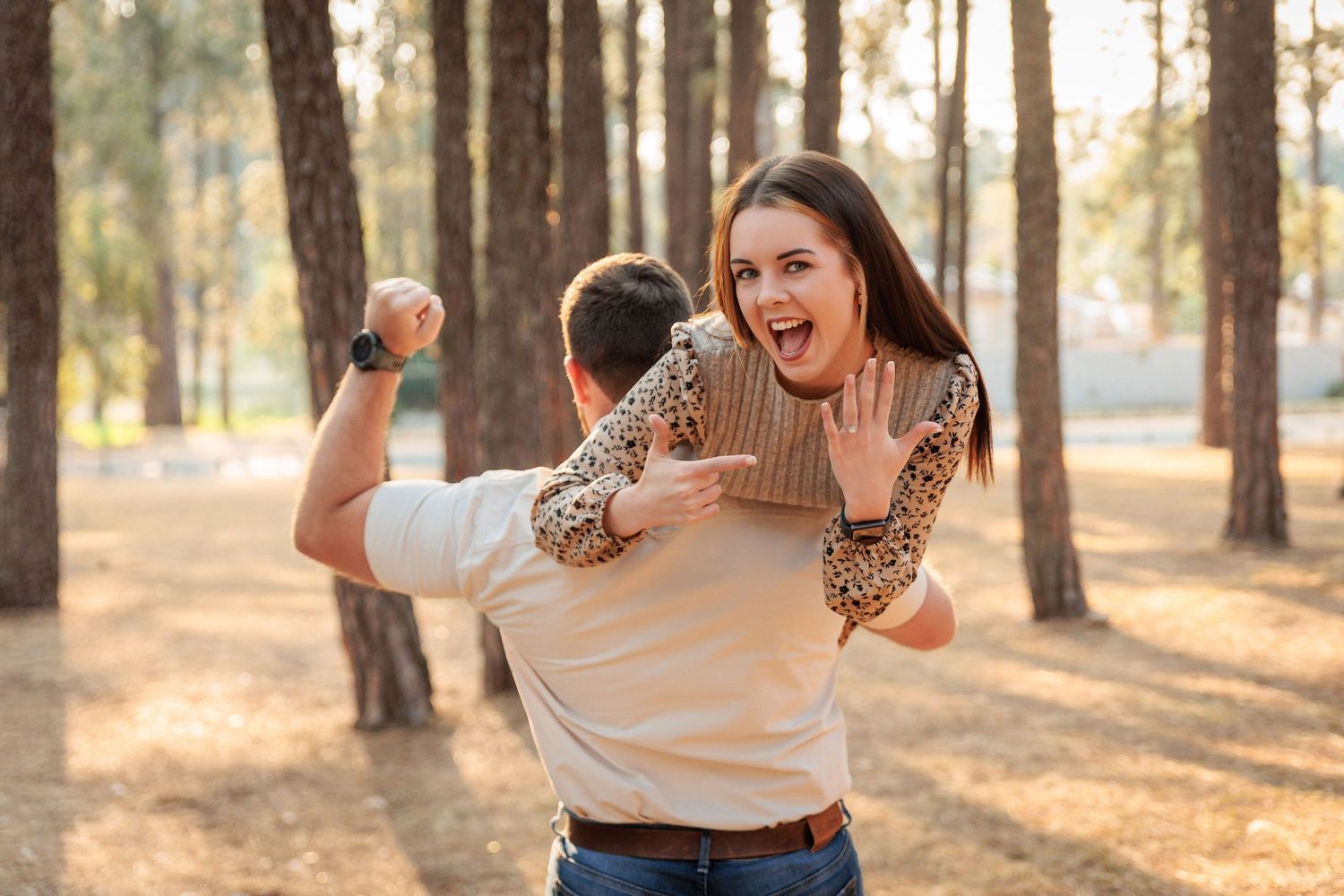 A playful couple in casual attire having fun in a sunlit forest during golden hour.