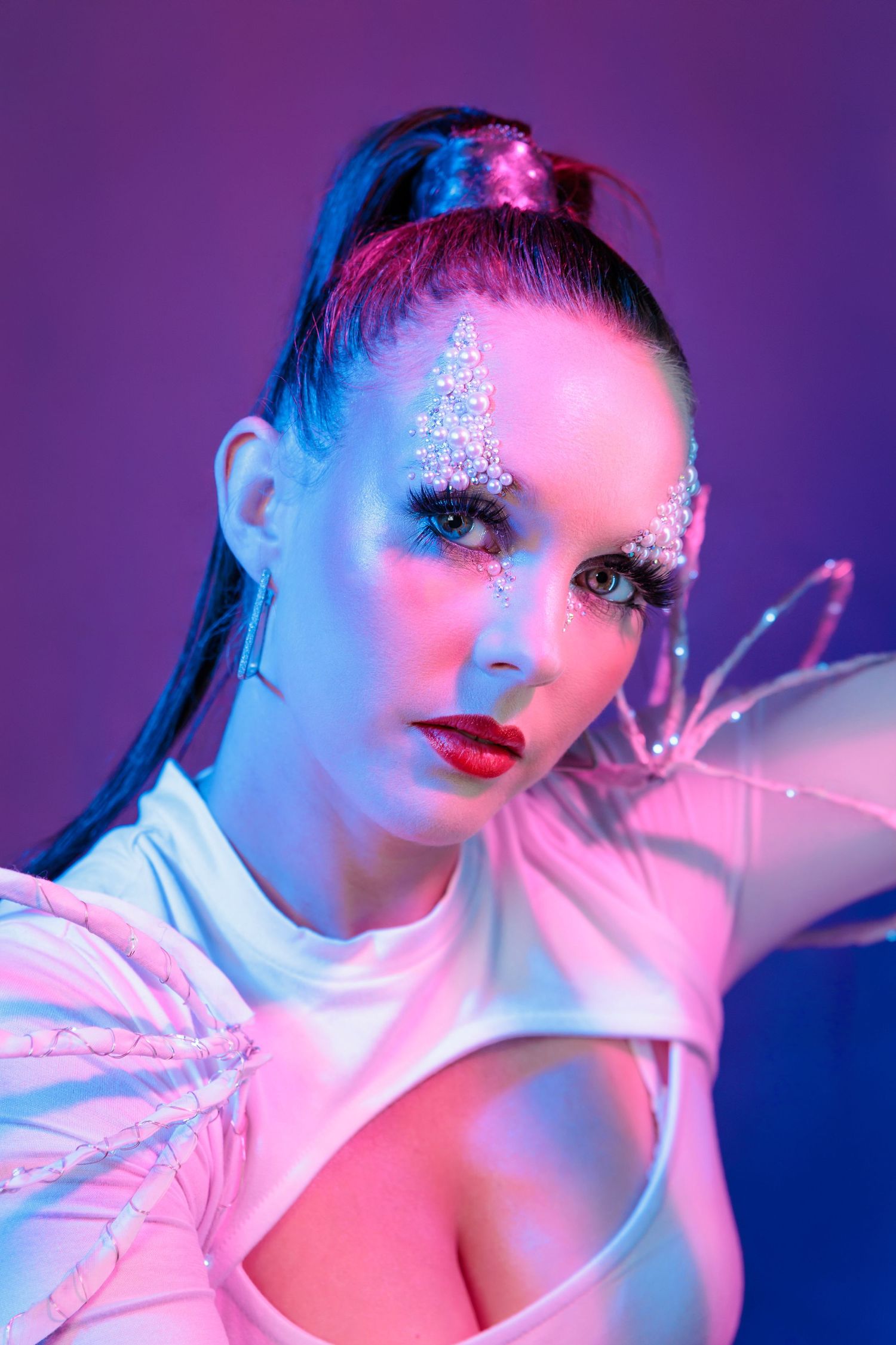 Artistic beauty portrait with glitter makeup, red lips and pink-blue lighting against purple background.