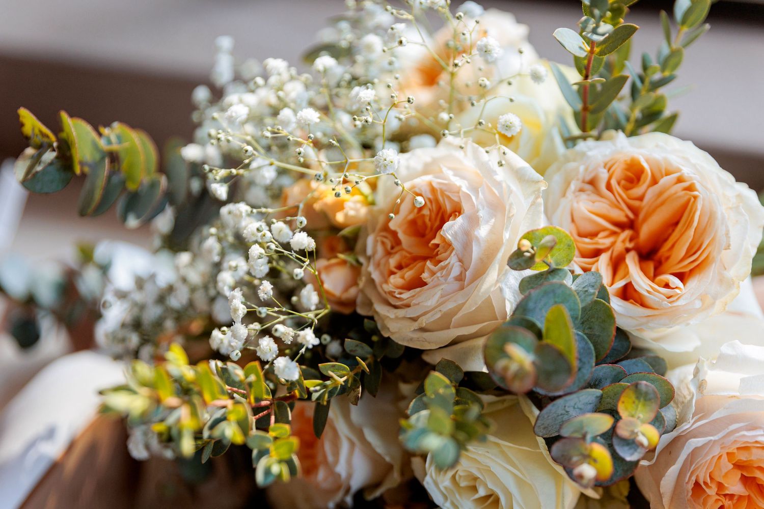 Romantic wedding bouquet featuring peach roses, baby's breath, and eucalyptus leaves.