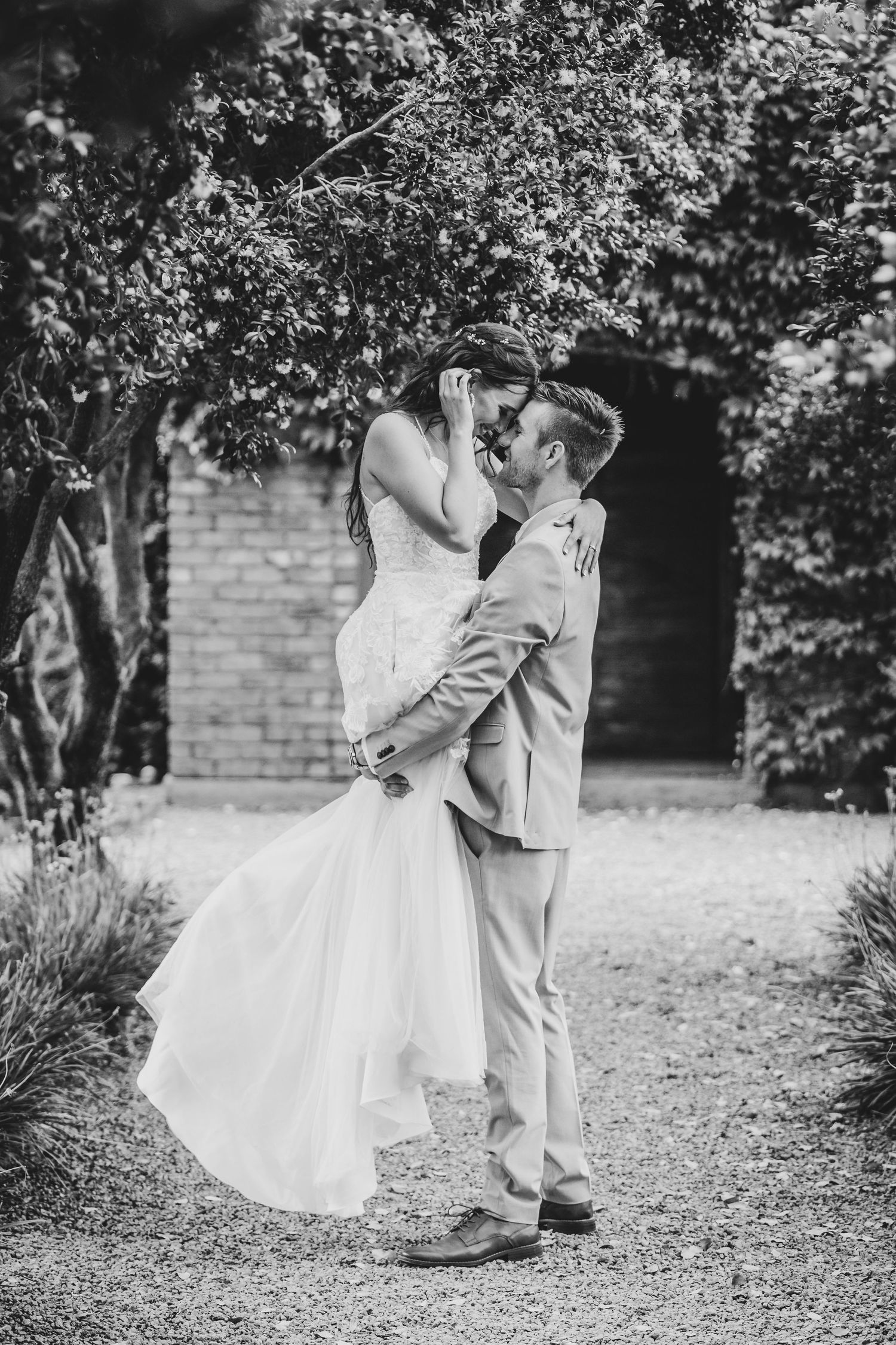 Black and white photo of a romantic wedding dance in a garden setting with brick walls.