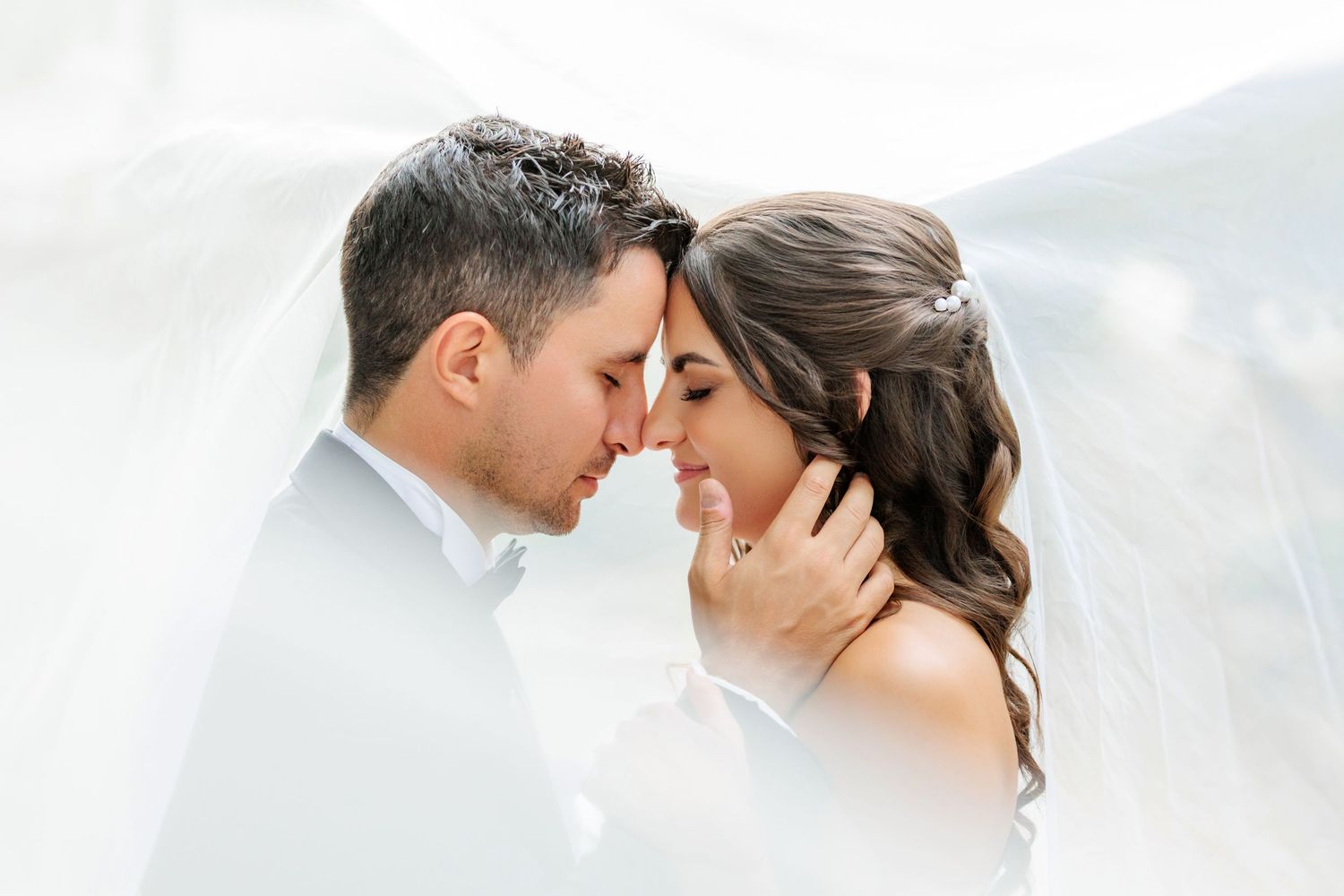 A romantic wedding couple embraces in soft sunlight during an intimate outdoor photo session.