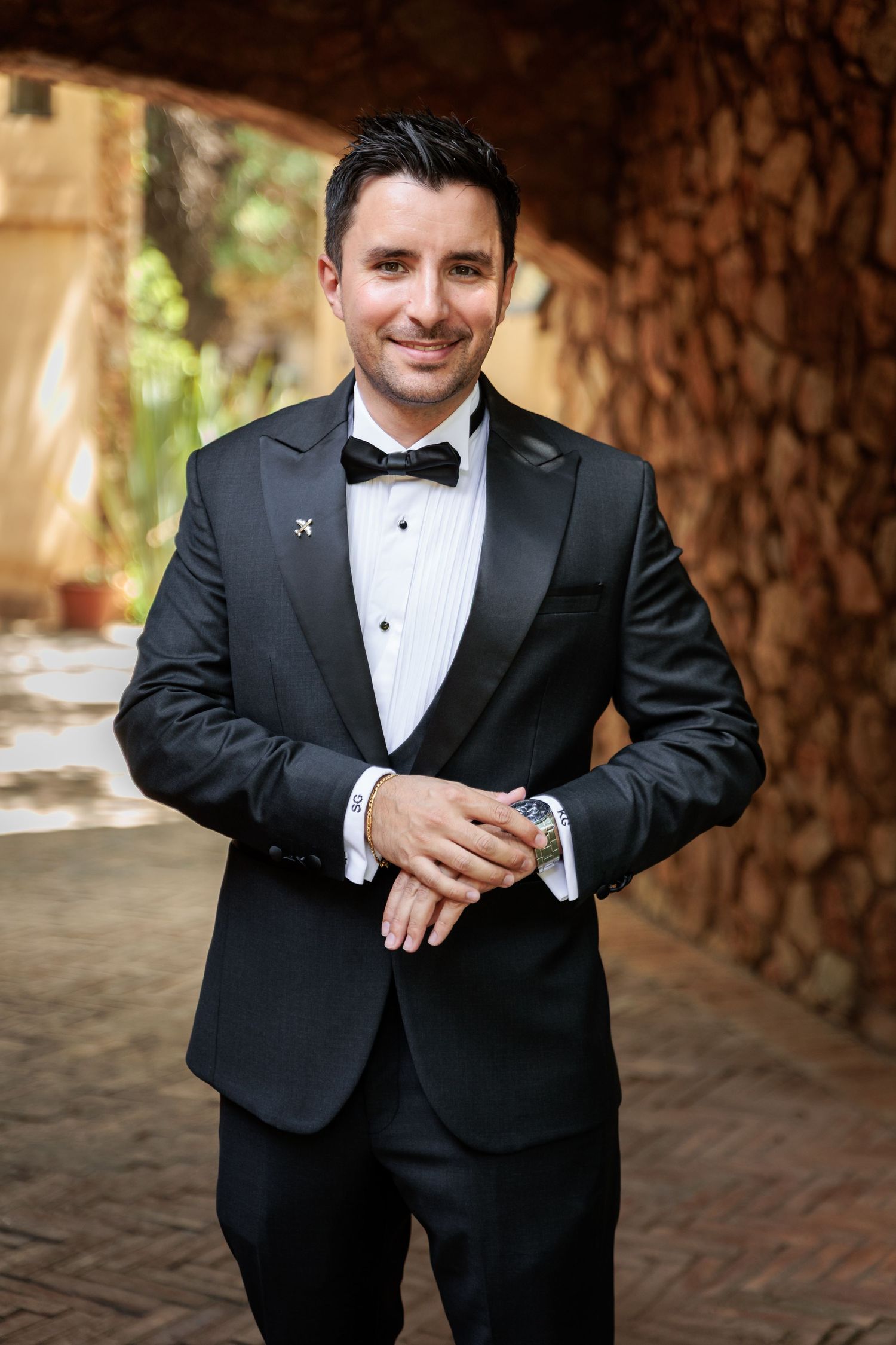 A person in a black tuxedo and bow tie poses in a brick archway during a formal event.