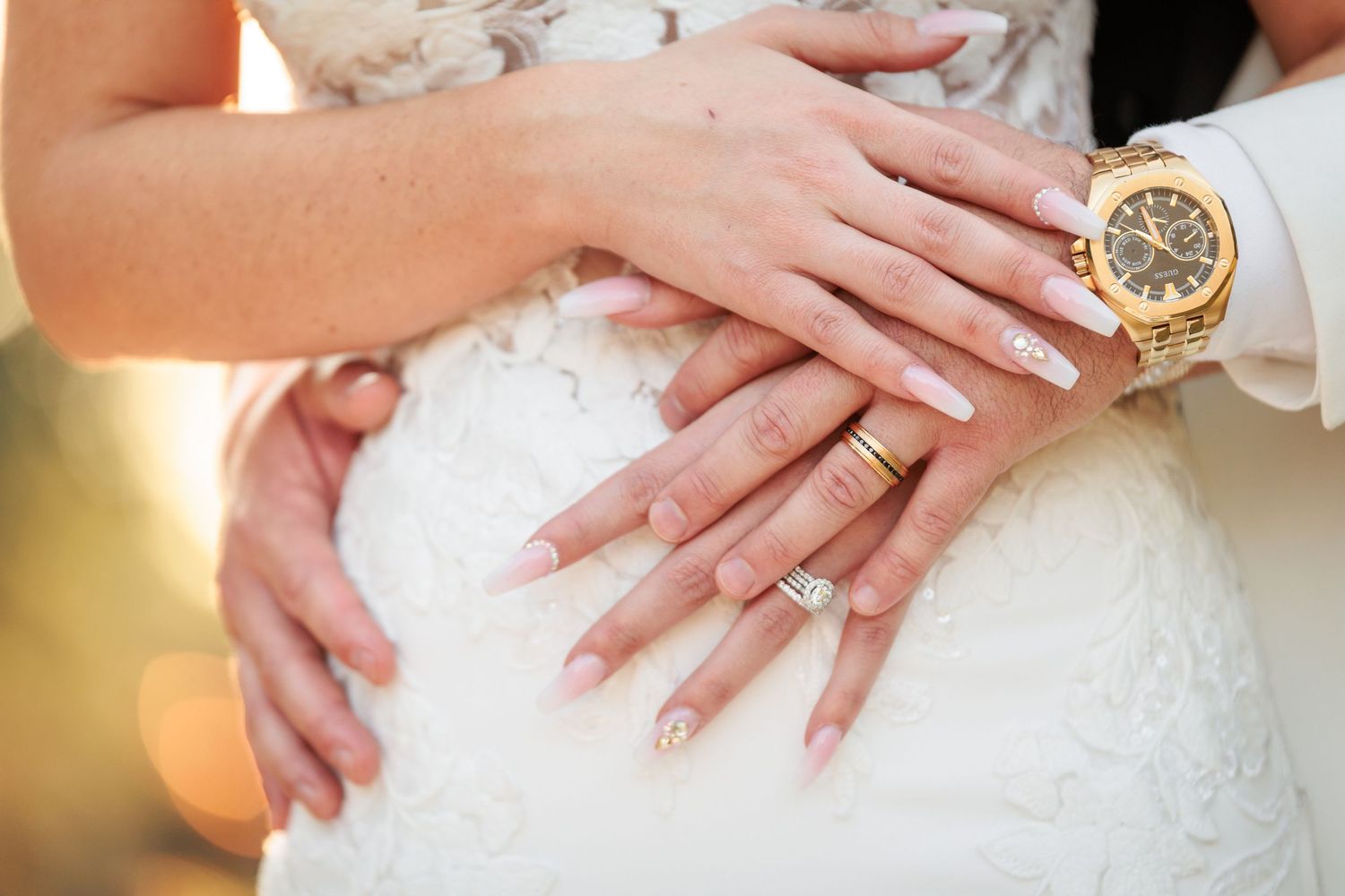 Close-up shot of hands displaying a diamond engagement ring on a white lace background.