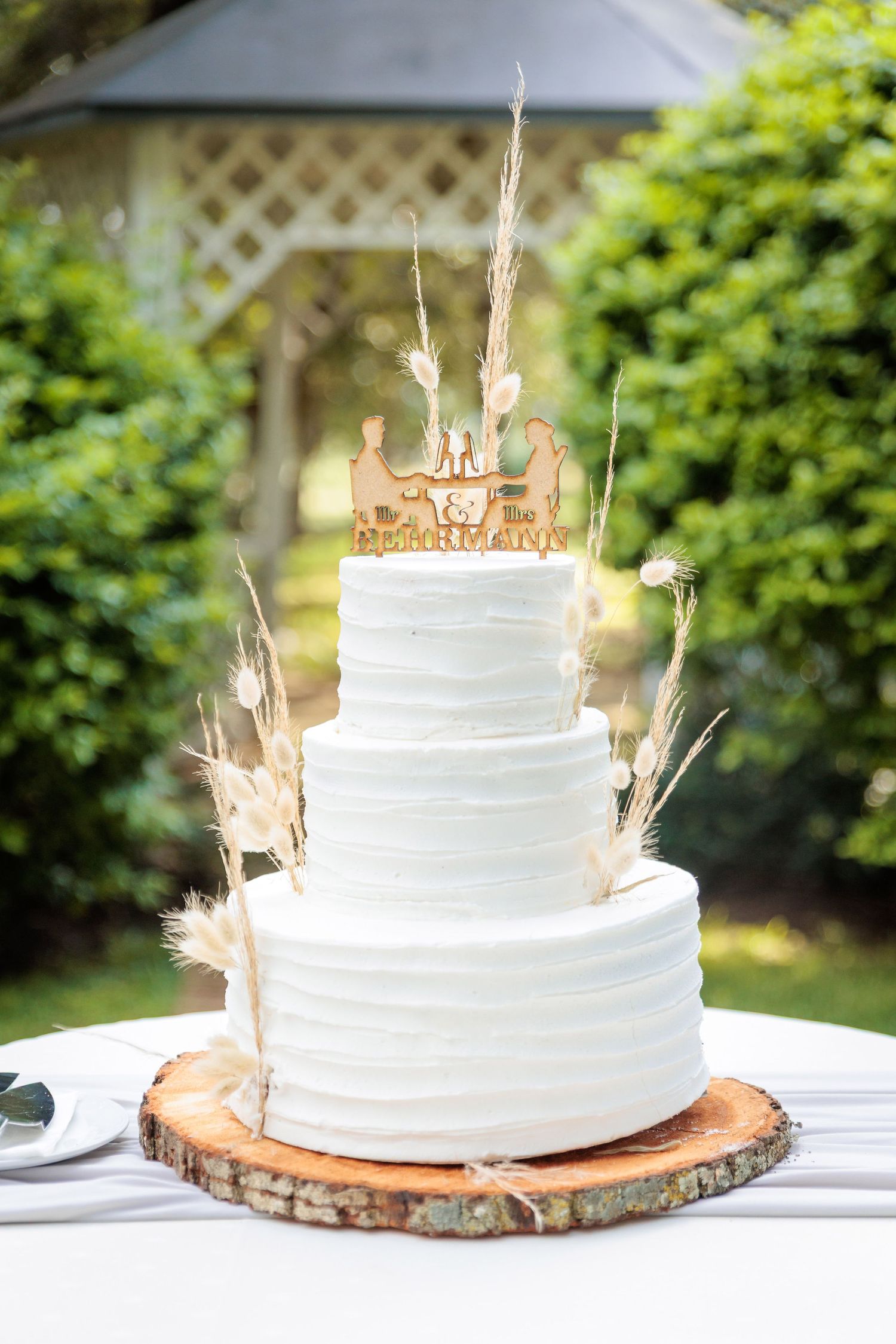 Three-tiered white wedding cake displayed on rustic wood slice.