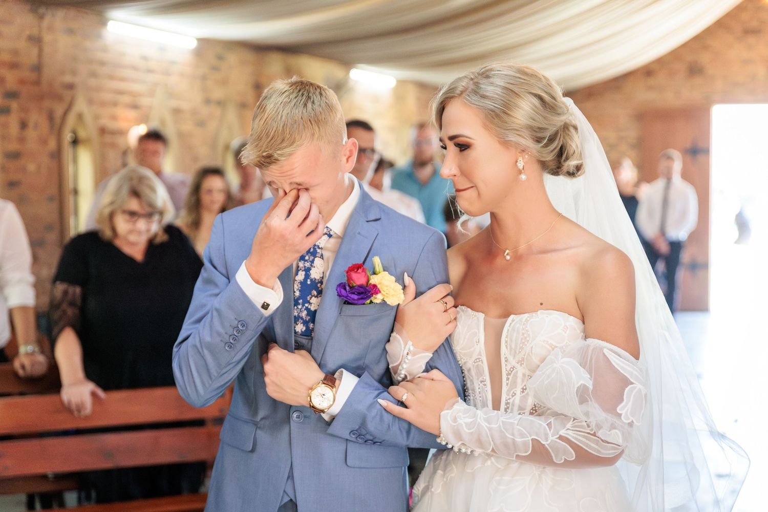 Emotional moment during wedding ceremony in brick chapel as couple shares touching reaction together at the altar.