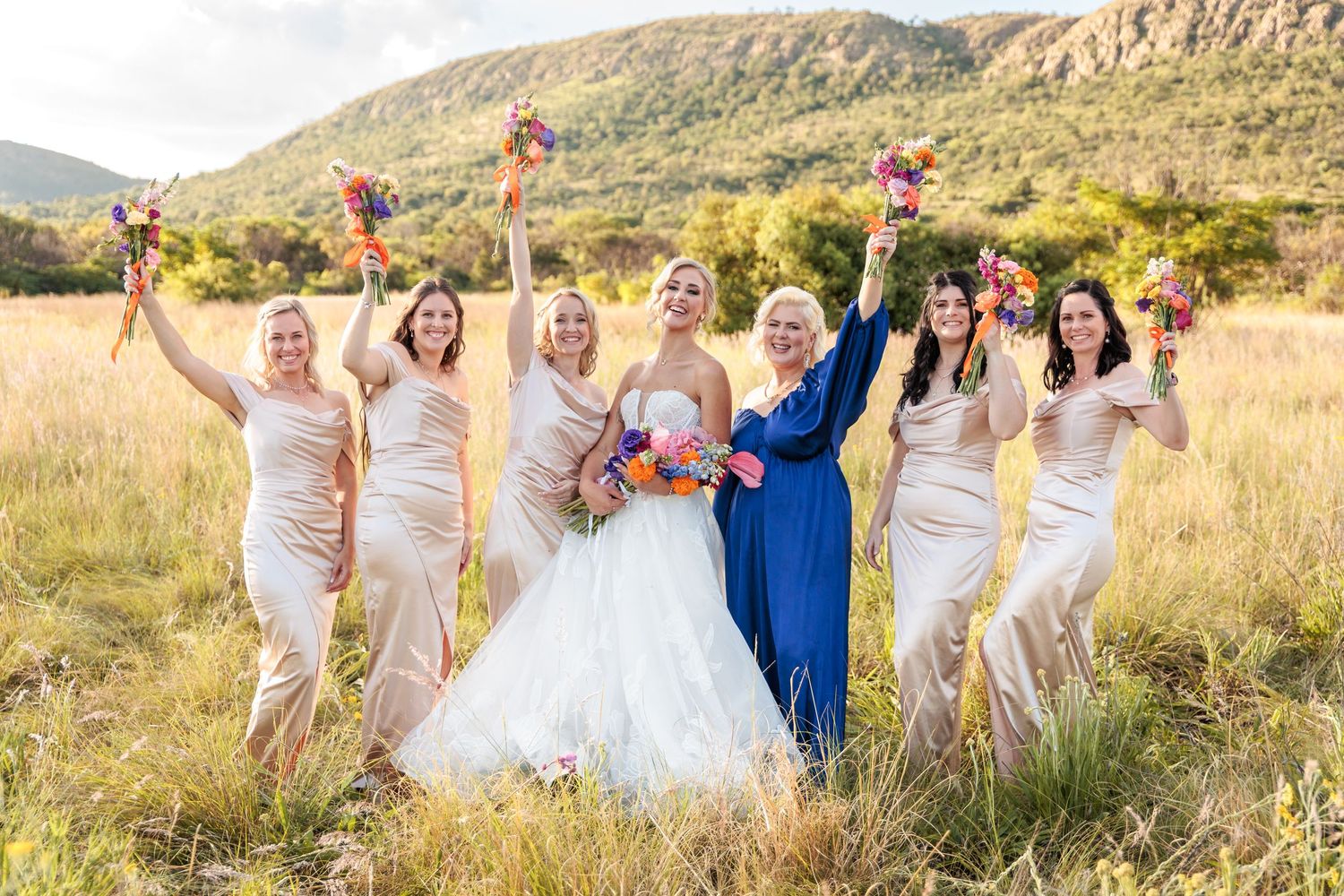 Wedding party celebrates joyfully against backdrop of scenic mountain landscape during golden hour.