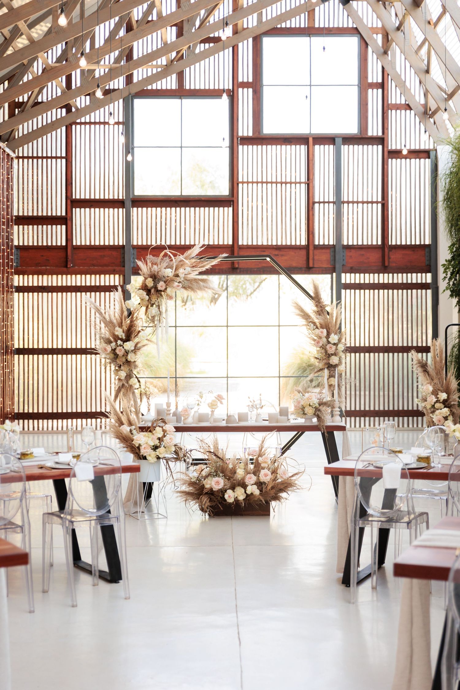 Modern barn venue interior with white floors, wooden beams, and elegant table settings for a rustic wedding reception.