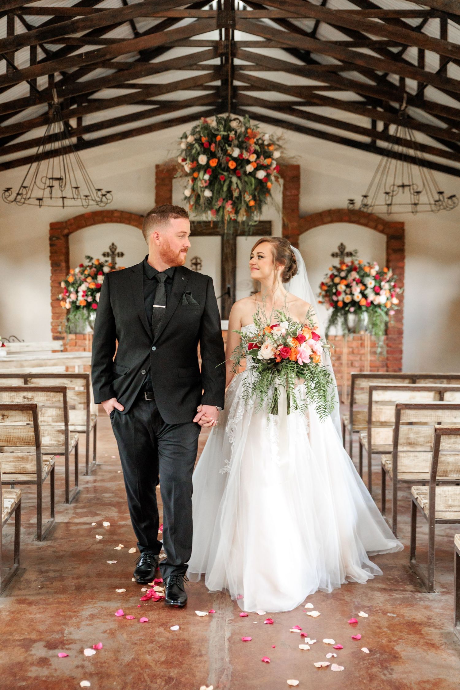 A couple shares a romantic moment in a rustic barn venue decorated with floral arrangements and scattered rose petals.