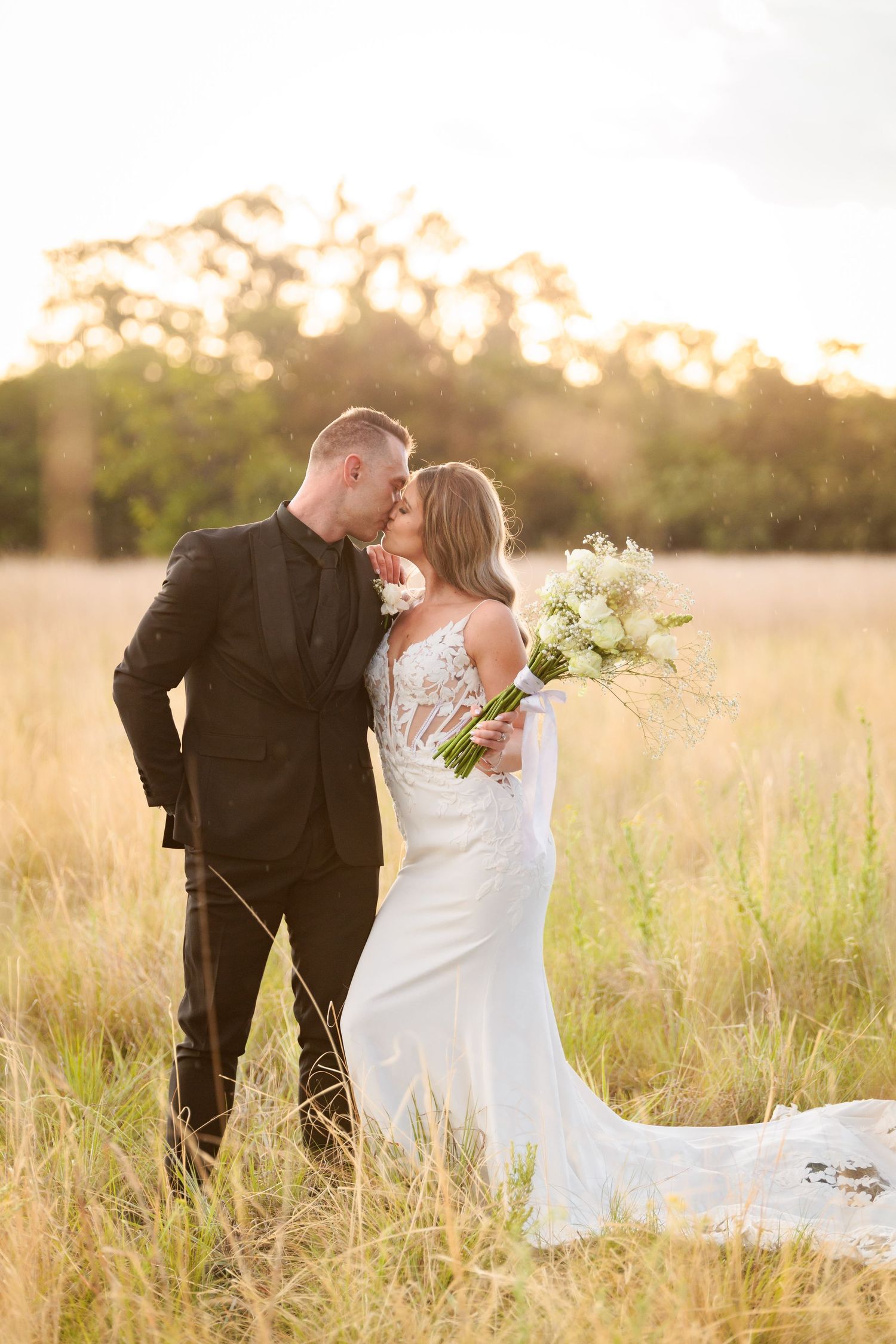 A couple shares an intimate moment in a golden field at sunset with the bride holding a white bouquet.